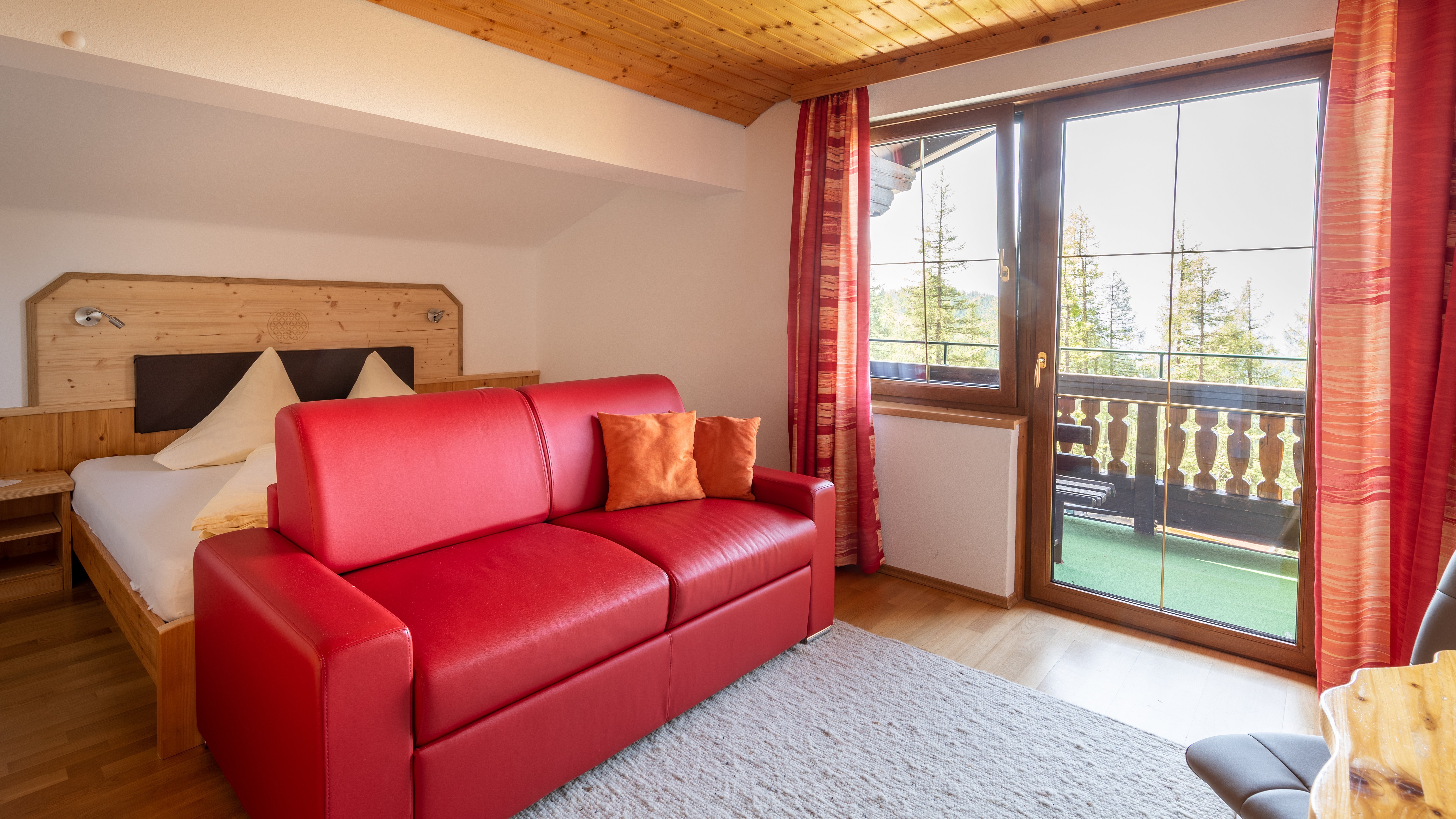 Hotelzimmer mit rotem Sofa, Holzverkleidungen und Fenster mit Blick auf Bäume im Freien