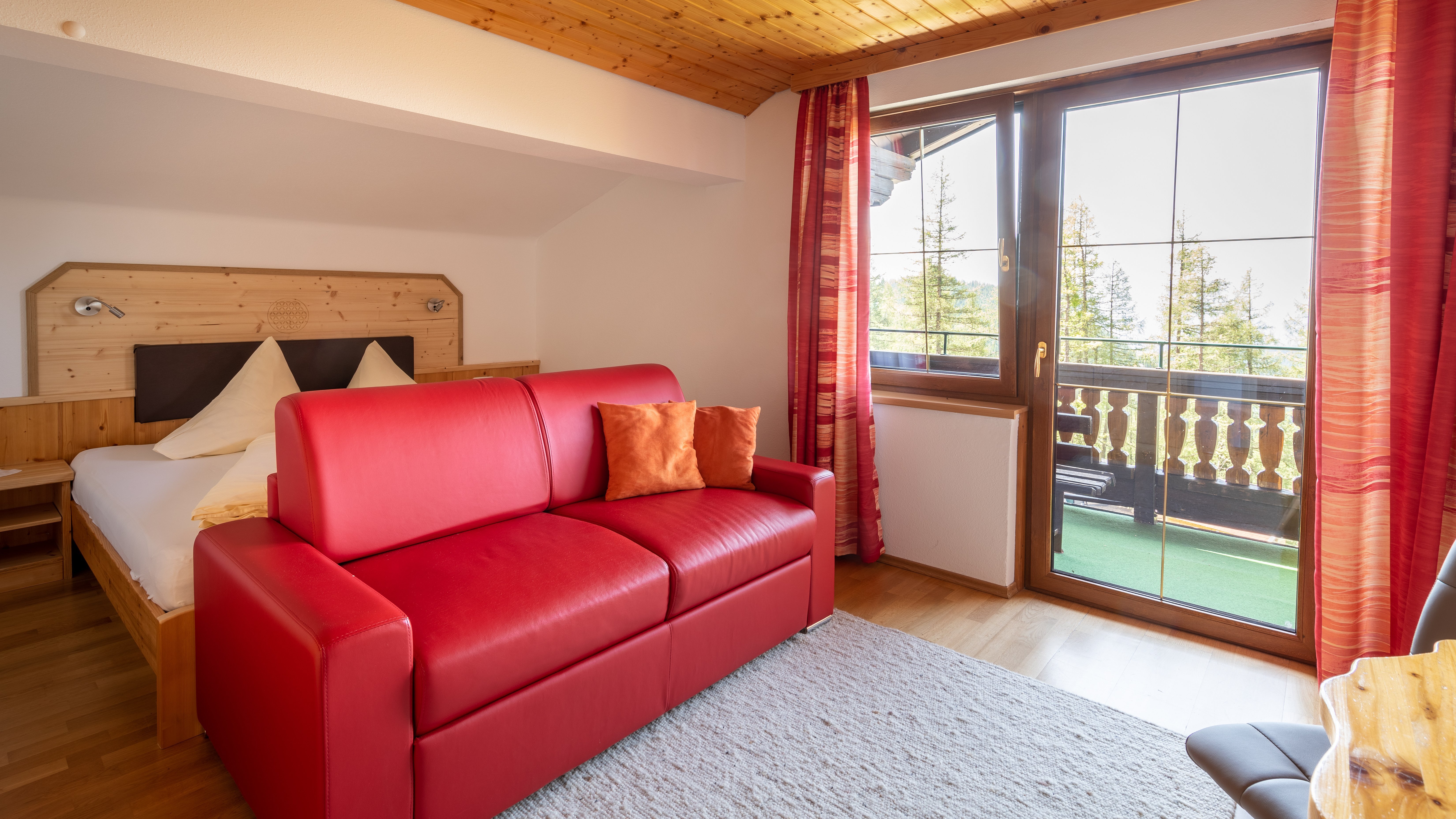 Hotelzimmer mit rotem Sofa, Holzverkleidungen und Fenster mit Blick auf Bäume im Freien