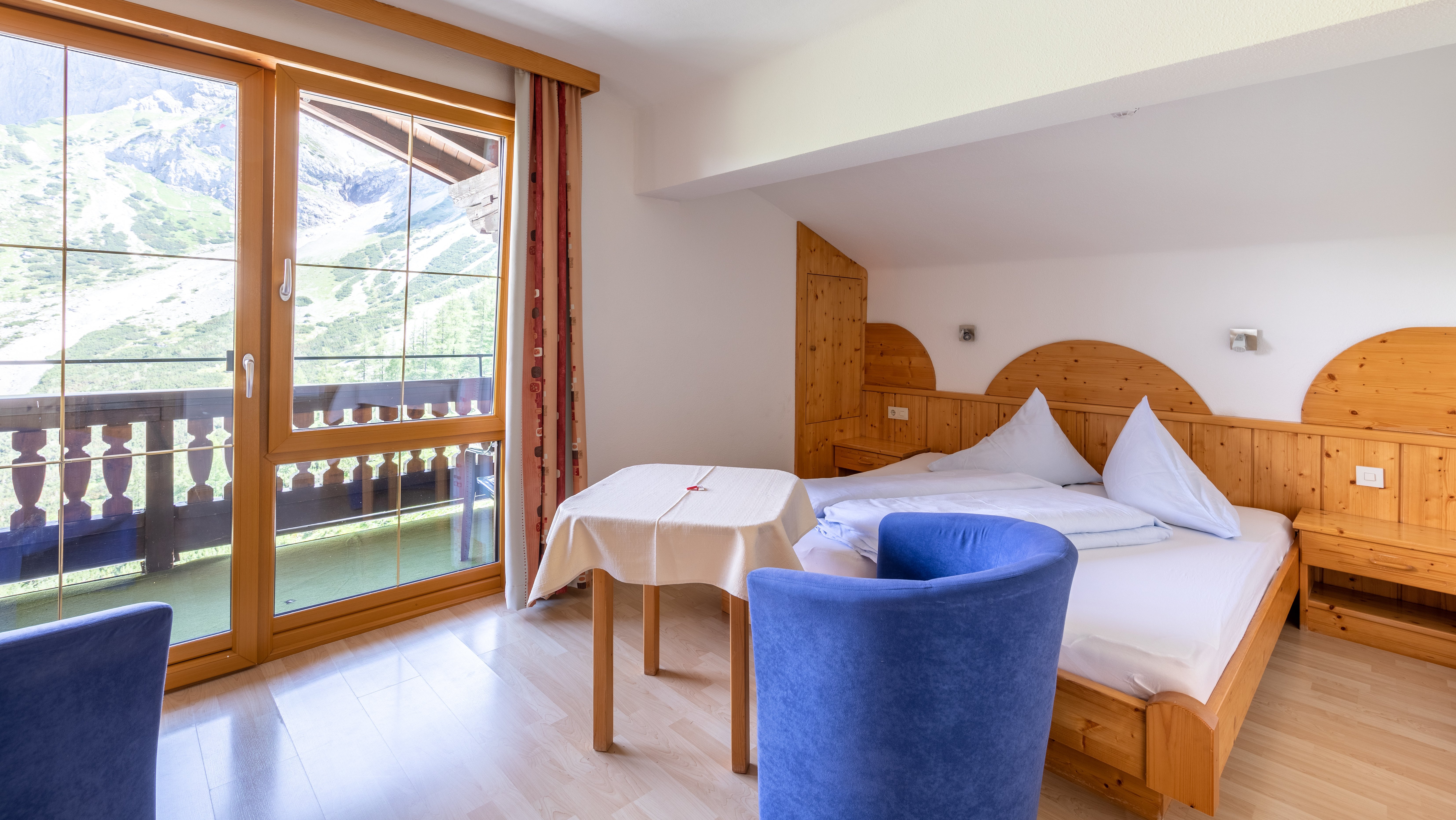 Ein einladendes Hotelzimmer mit großem Bett, Tisch und Stühlen sowie Fenster mit Blick auf die Berge.