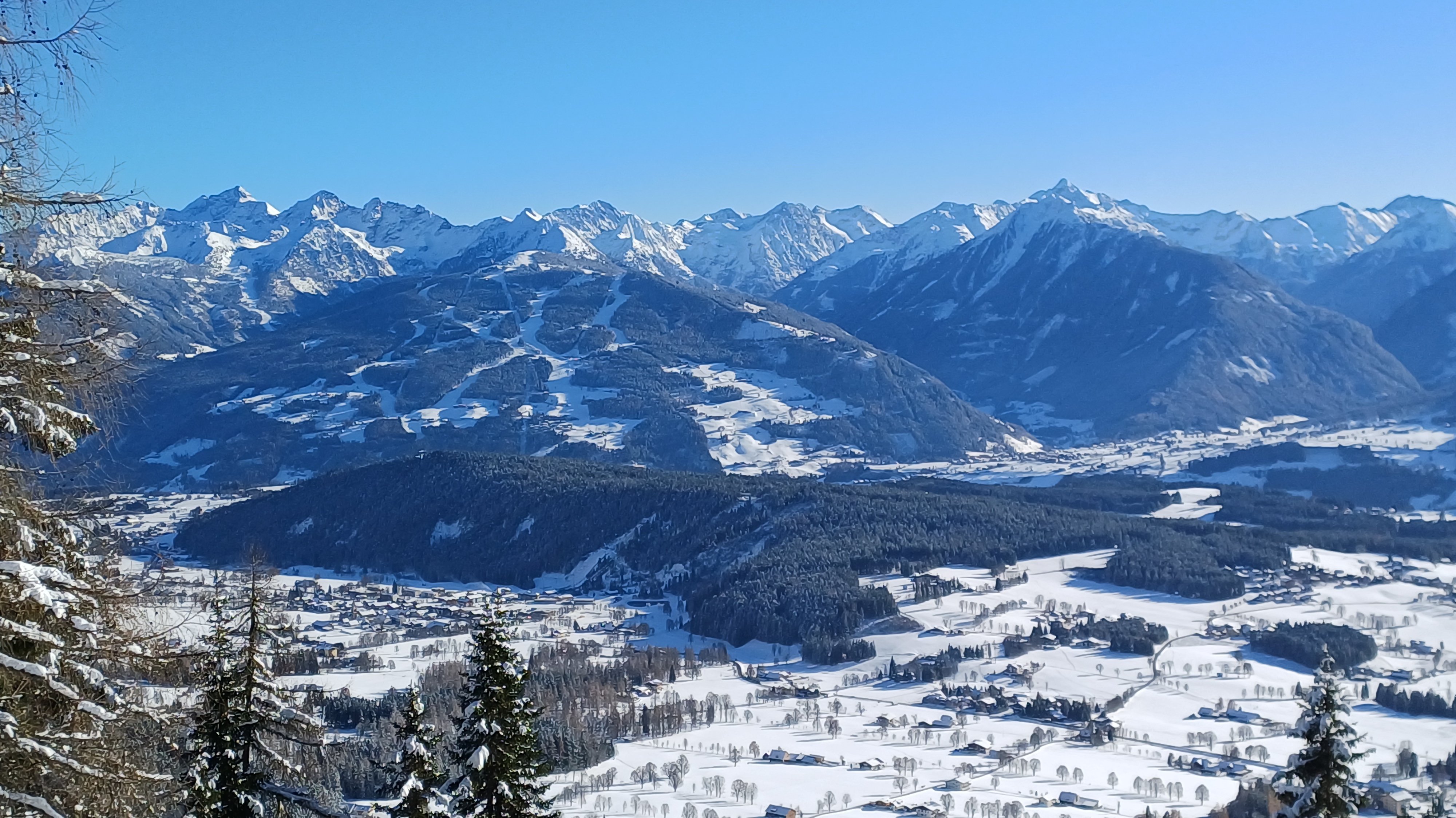 Schneeüberzogene Berglandschaft mit Tal und kleinem Ort unter blauem Himmel in den Alpen.