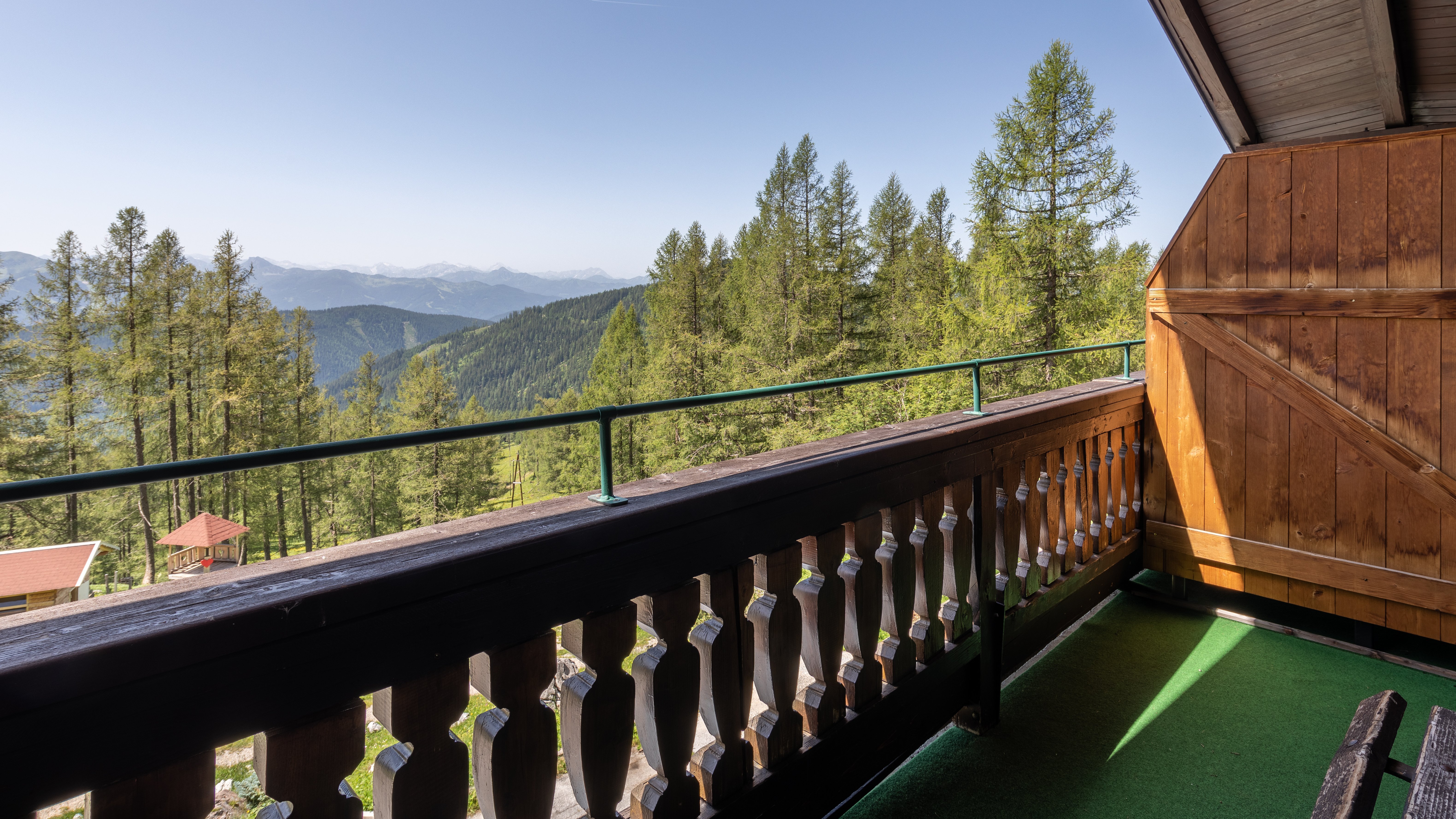 Balkon mit Holzgeländer und Blick auf eine Berglandschaft mit Bäumen und Gipfeln unter klarem Himmel