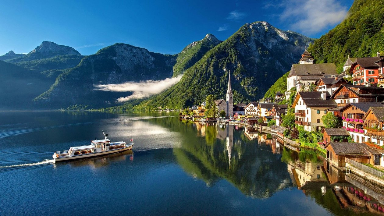 Idyllisches Dorf am See Landschaft mit See und Bergdorf, Boot auf dem Wasser und Spiegelung der Gebäude im See