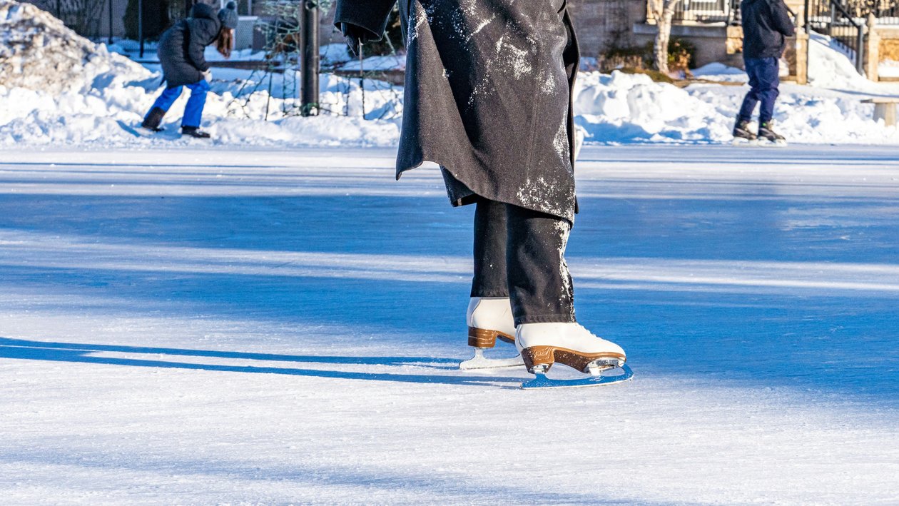 Eislaufvergnügen auf dem gefrorenen See Person beim Eislaufen auf einer gefrorenen Fläche mit Skatern im Hintergrund und schneebedecktem Umland