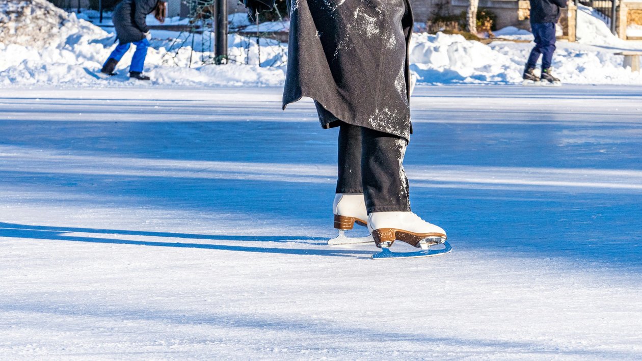 Eislaufvergnügen auf dem gefrorenen See Person beim Eislaufen auf einer gefrorenen Fläche mit Skatern im Hintergrund und schneebedecktem Umland
