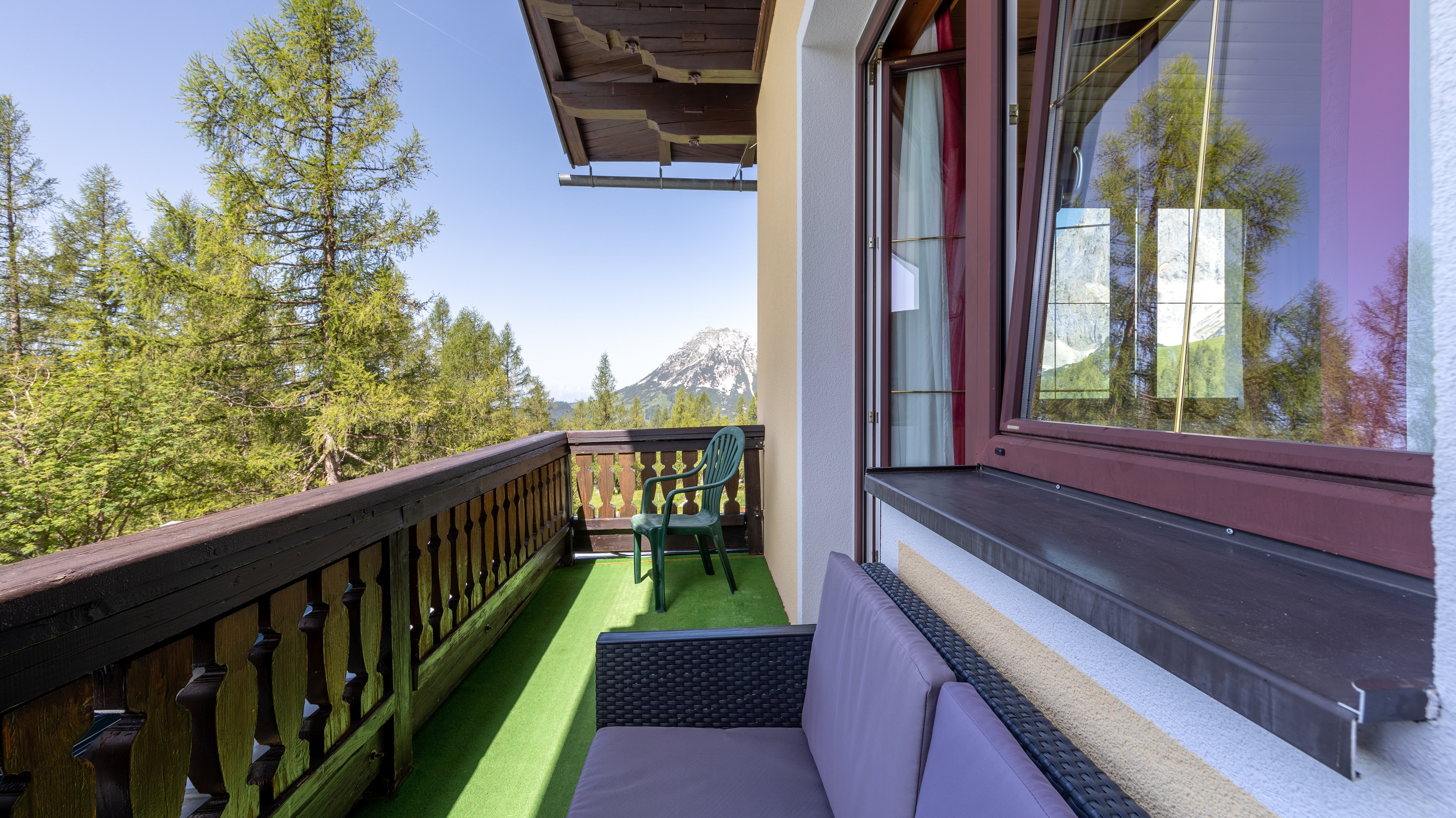 Balkon mit Sitzgelegenheiten und Blick auf die Berge, umgeben von Bäumen und Natur.