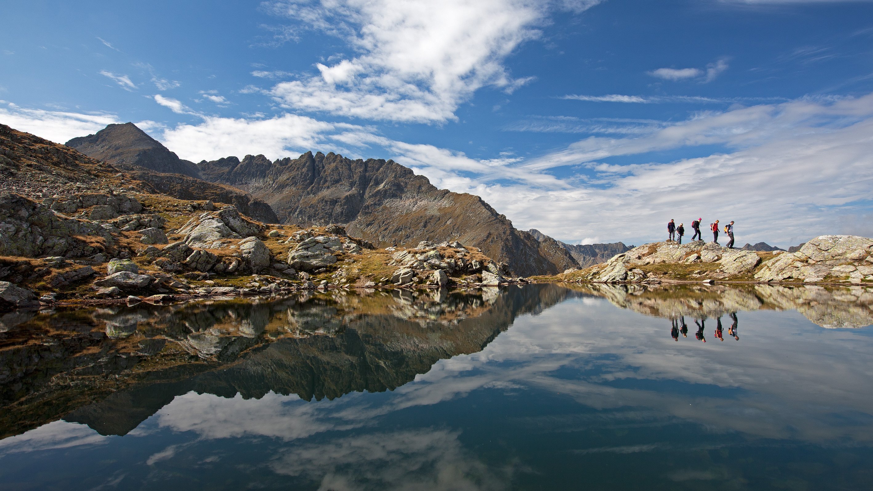 Naturerlebnis beim Wandern in den Bergen Gruppe von Wanderern am Ufer eines ruhigen Sees mit reflektierenden Bergen im Hintergrund