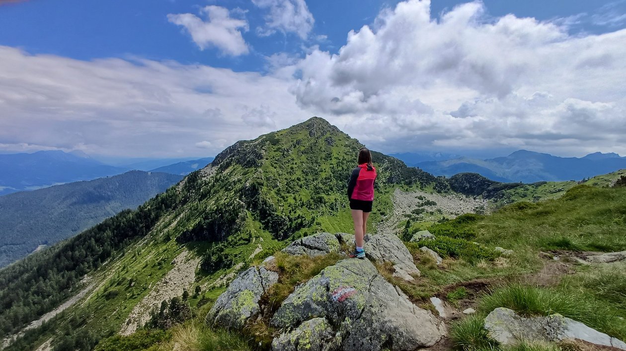 Faszinierende Berglandschaft entdecken Eine Person steht auf einem Felsen und blickt auf grüne Berge unter einem teils bewölkten Himmel.