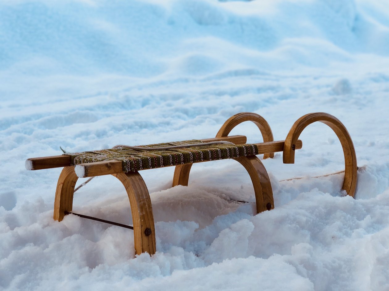 Ein hölzerner Schlitten liegt in einer verschneiten Landschaft umgeben von frisch gefallenem Schnee.