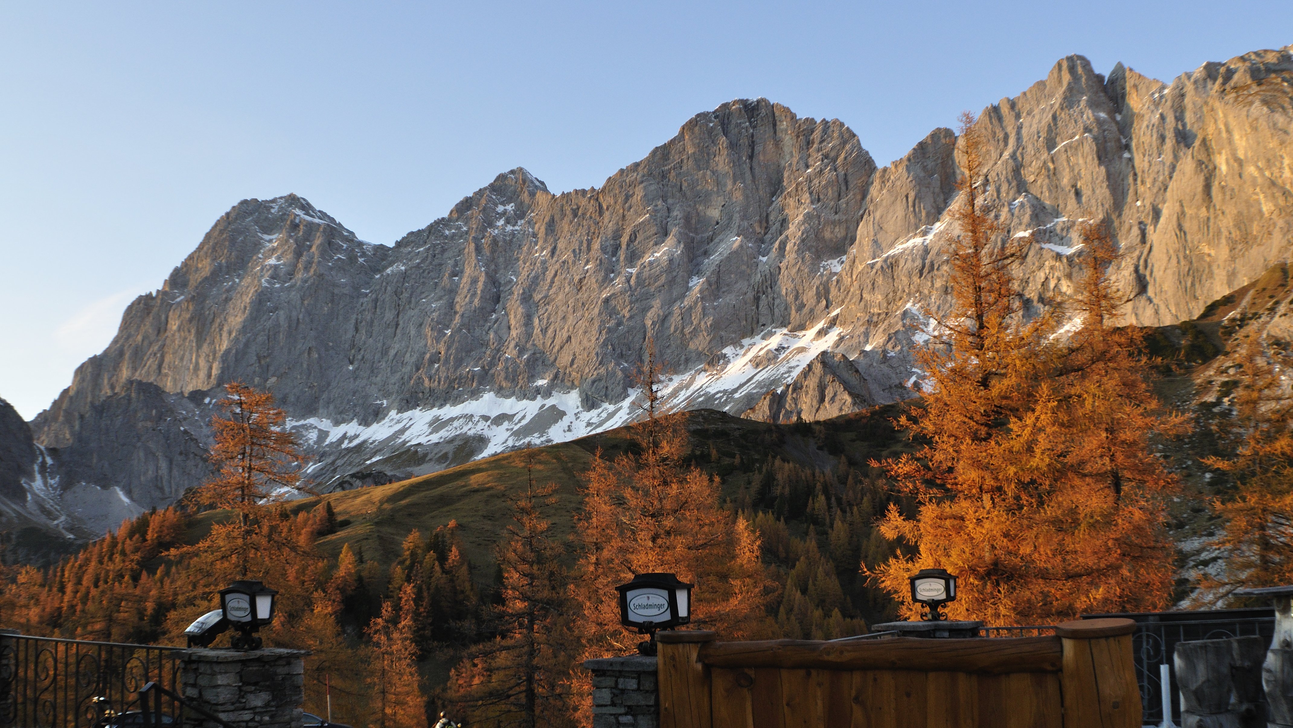 Berglandschaft mit herbstlichen Bäumen und felsigen Gipfeln unter klarem Himmel.