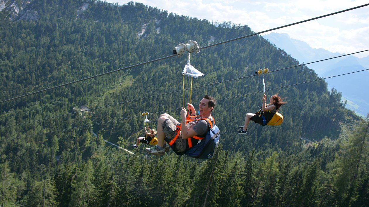 Zipline Abenteuer im Bergland Zwei Personen beim Ziplining über eine bergige Landschaft mit Bäumen und weitem Blick
