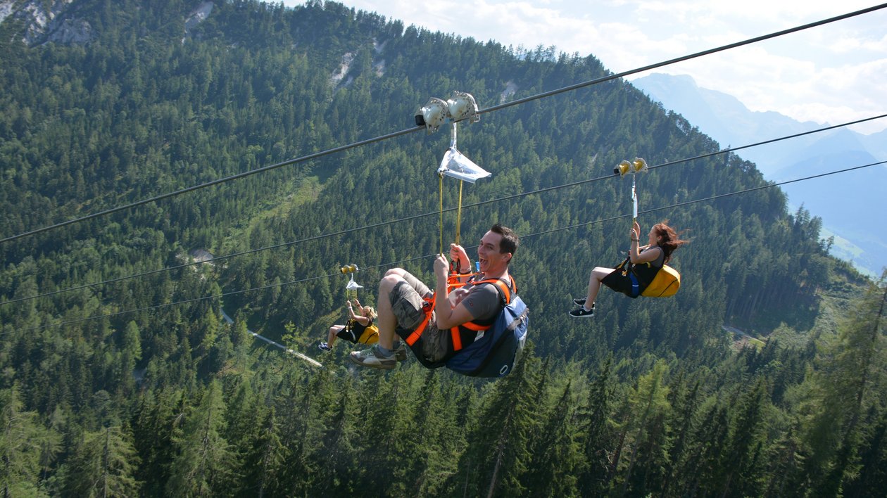 Zipline Abenteuer im Bergland Zwei Personen beim Ziplining über eine bergige Landschaft mit Bäumen und weitem Blick