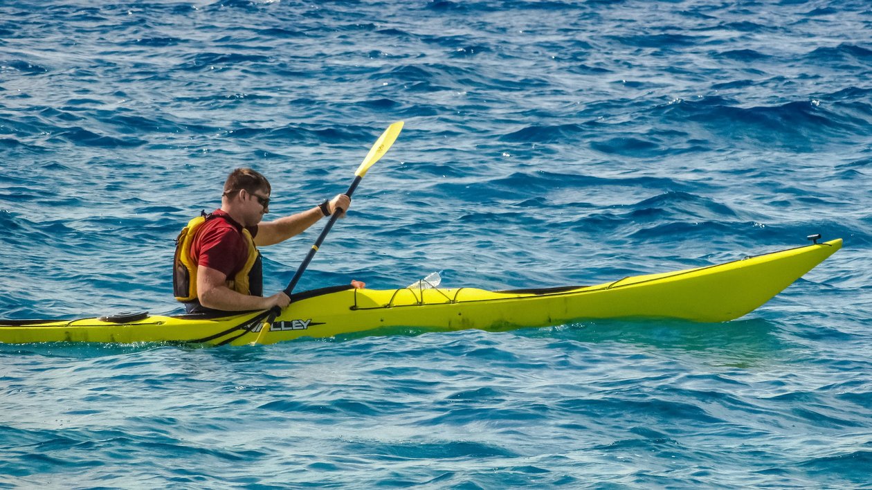 Abenteuer beim Kajakfahren Eine Person paddelt in einem gelben Kajak auf ruhigem Wasser mit Paddel in der Hand.