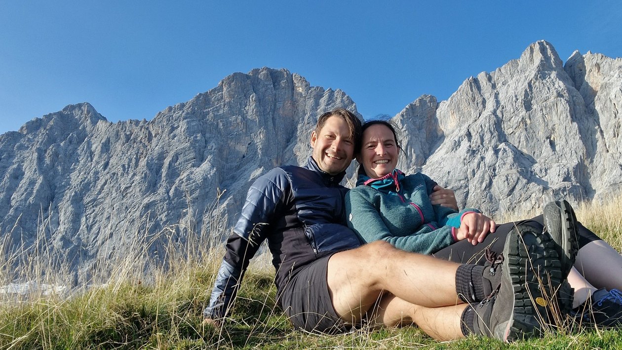 Bergromantik in den Alpen Ein Paar sitzt auf einer Wiese in den Bergen unter einem blauen Himmel und genießt die Natur.