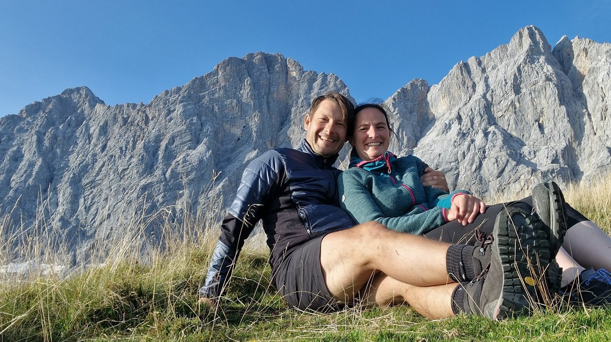 Bergromantik in den Alpen Ein Paar sitzt auf einer Wiese in den Bergen unter einem blauen Himmel und genießt die Natur.