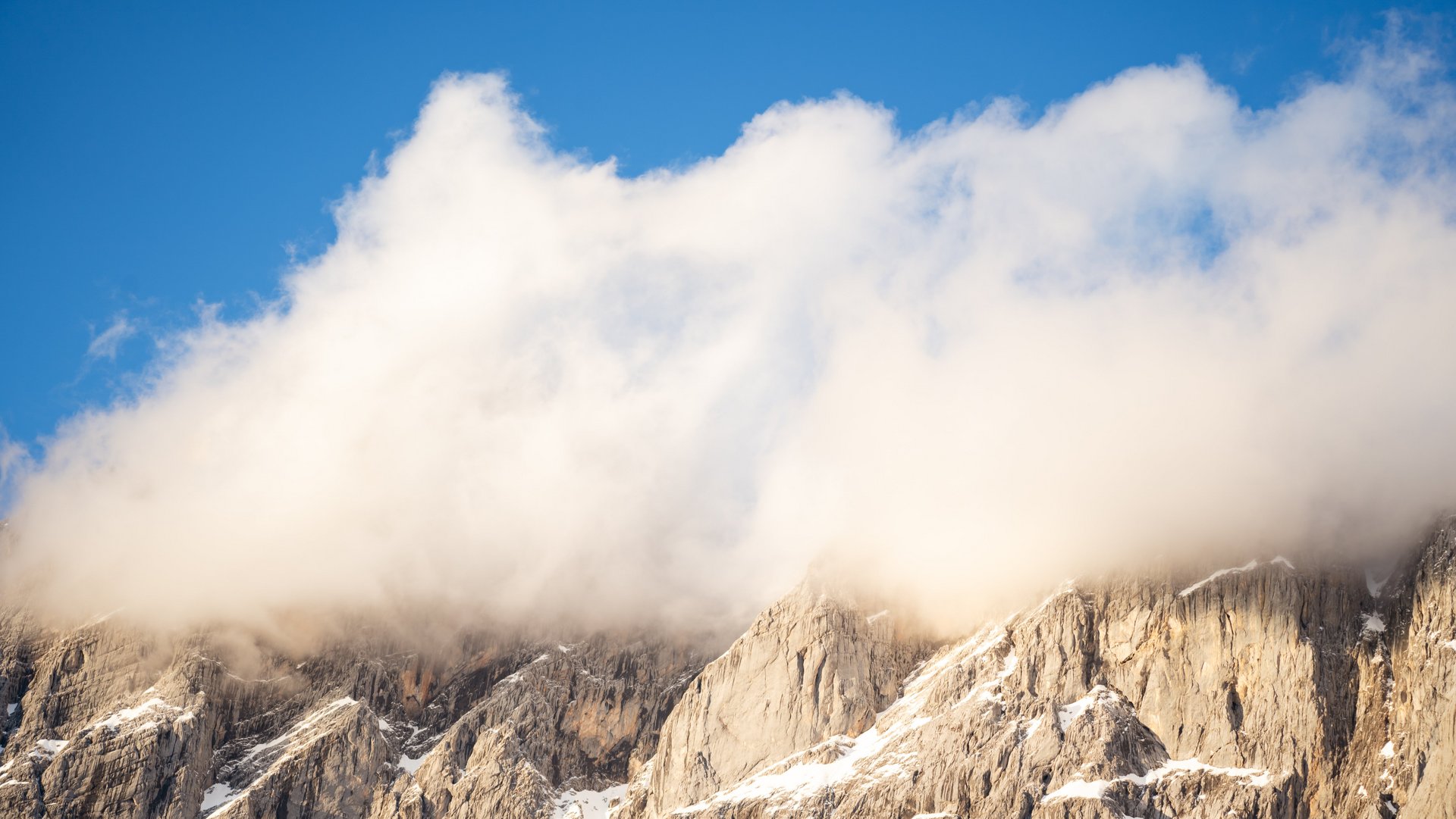 Rugged mountain peaks partially covered by clouds under a clear sky, natural landscape