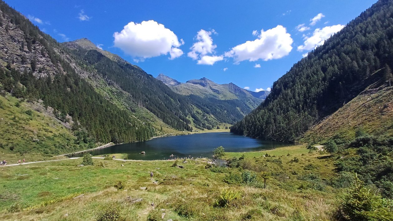 Idyllischer Bergsee in der Natur Bergsee umgeben von grünen Hügeln und Bergen unter blauem Himmel mit Wolken, Outdoor Landschaft