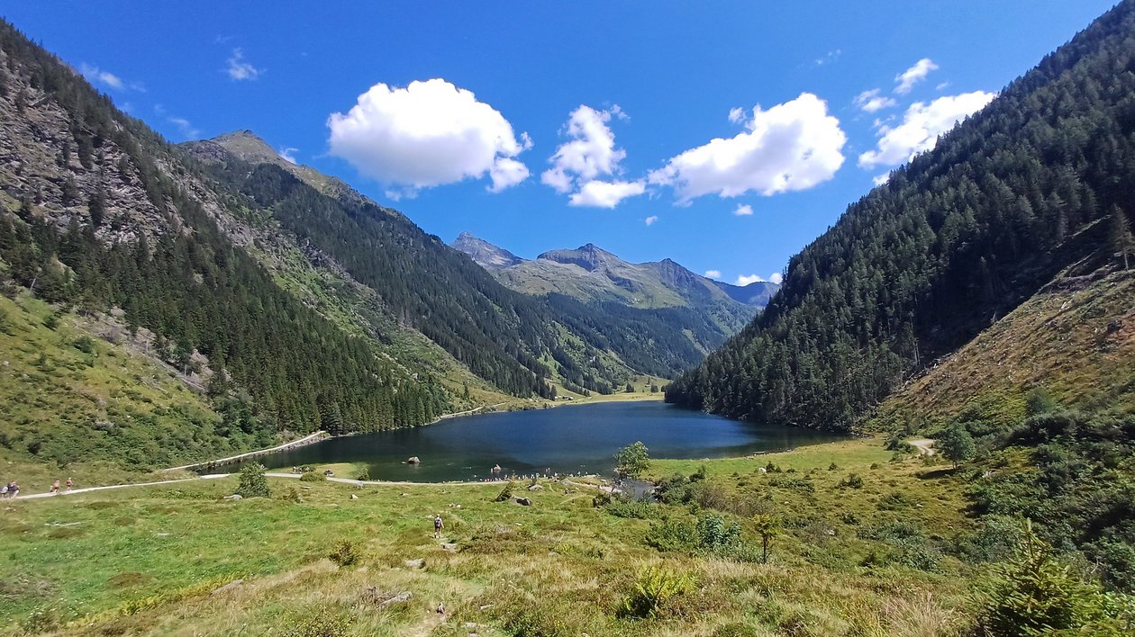 Idyllischer Bergsee in der Natur Bergsee umgeben von grünen Hügeln und Bergen unter blauem Himmel mit Wolken, Outdoor Landschaft