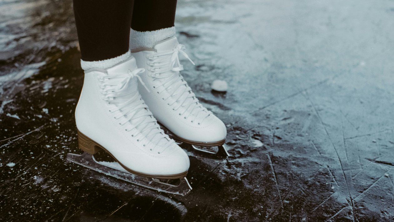 Eislaufen im Winterparadies Ein Paar weiße Eislaufschuhe steht auf einer glatten Eisfläche im Freien vor winterlicher Kulisse.