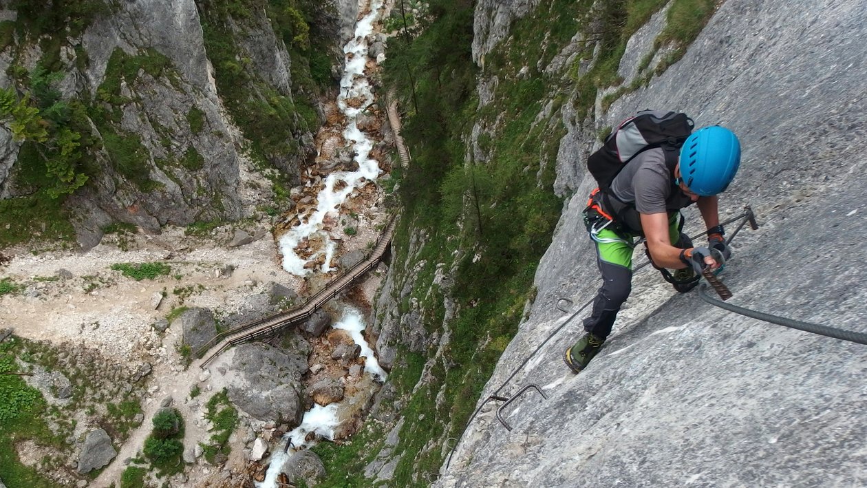 Abenteuerliches Klettern in der Berglandschaft Kletterer erklimmt eine Felswand mit einem Fluss im Hintergrund und Berge umgeben ihn.