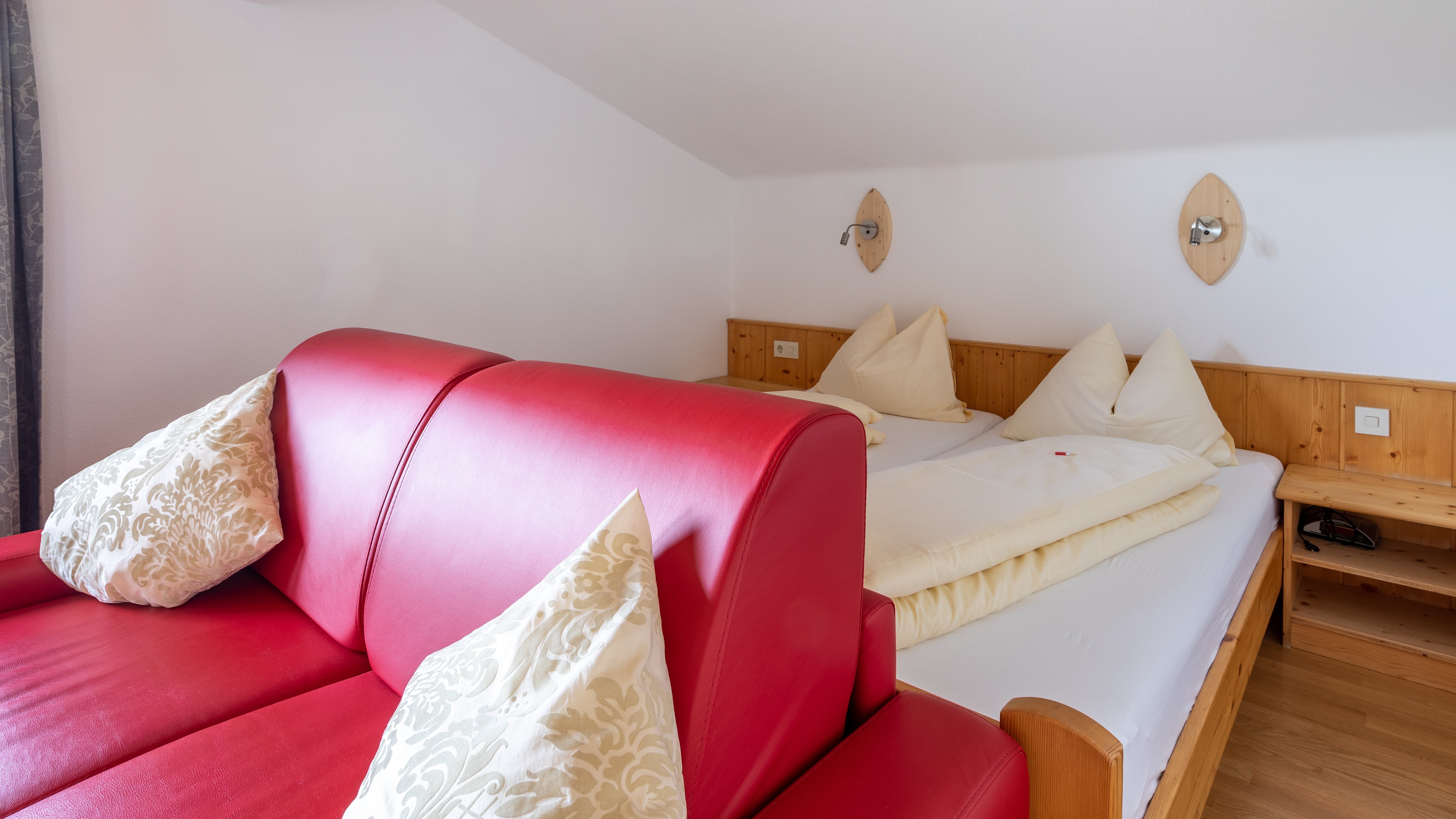 Kuscheliges Hotelzimmer mit rotem Sofa und dekorativen Kissen auf dem Bett. Möbel und stilvolle Einrichtung sichtbar.