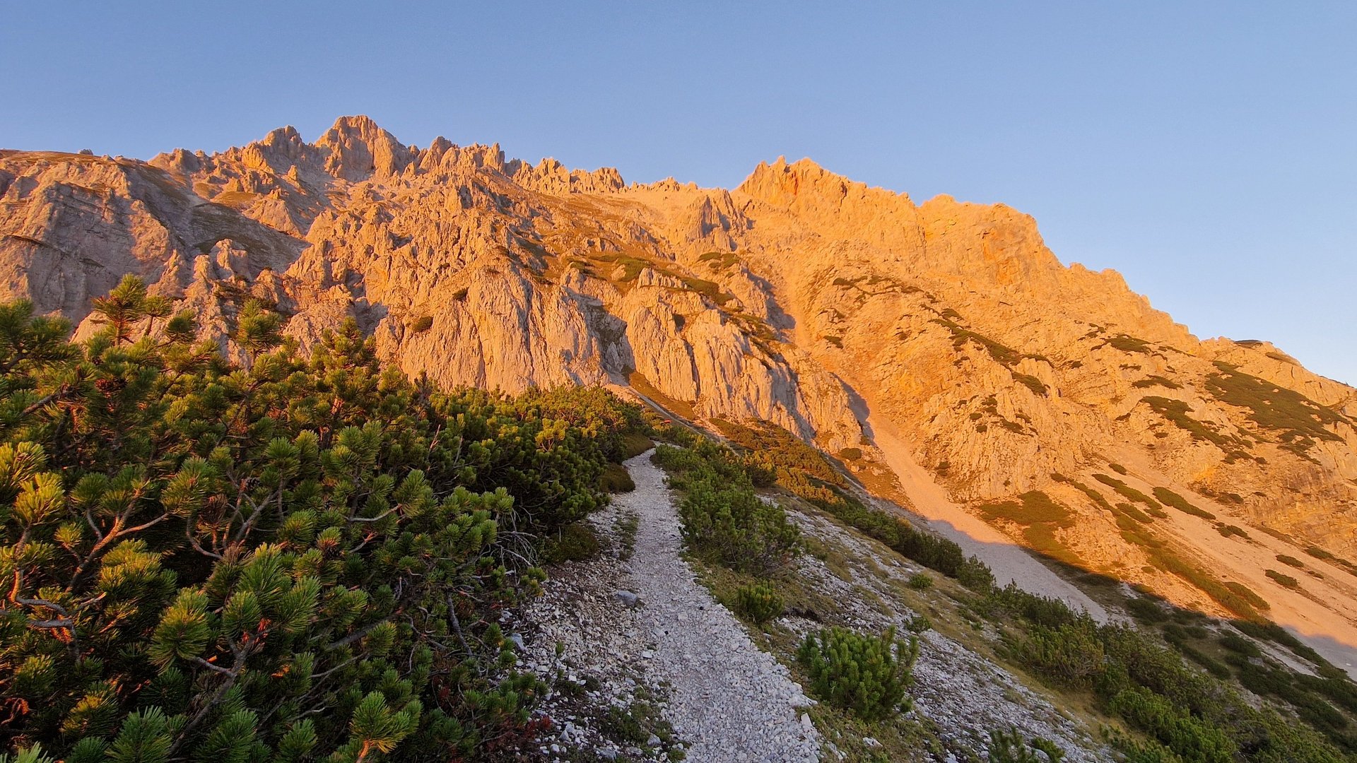 Berglandschaft mit Felsformationen und einem Wanderweg bei Sonnenaufgang, umgeben von Natur.