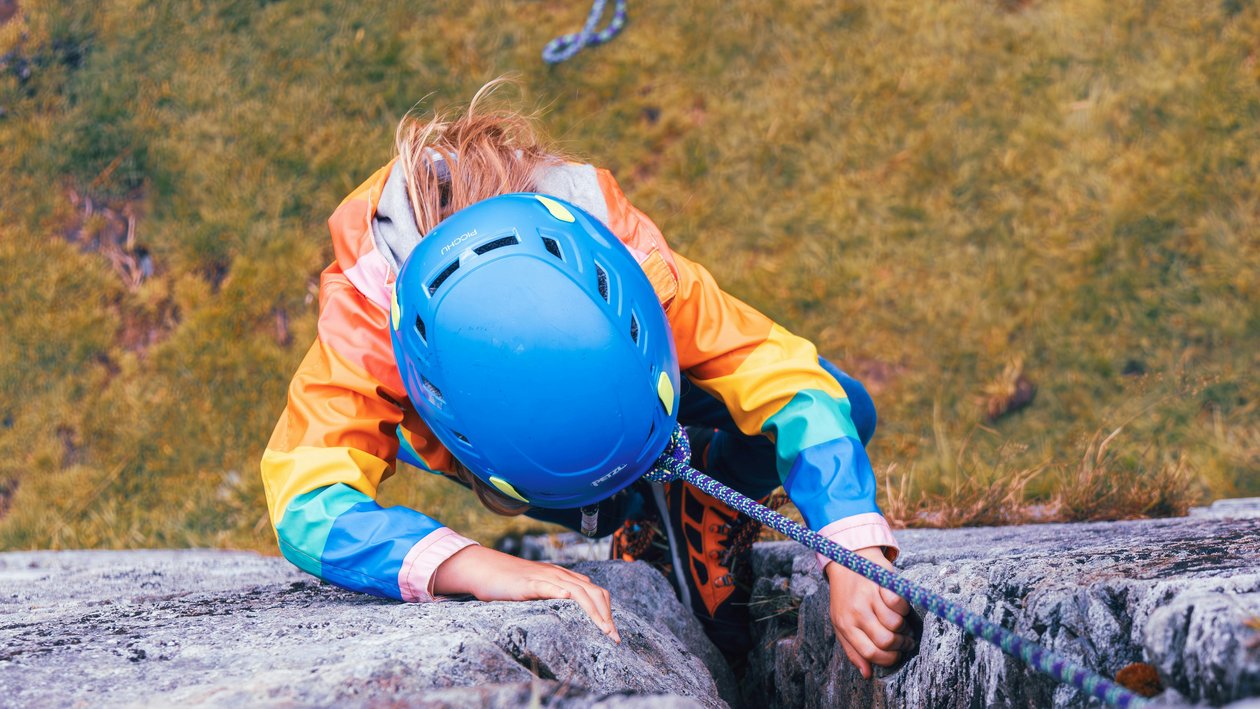 Abenteuerliches Klettern in den Bergen Eine Person klettert an einer Felswand mit bunter Jacke und blauem Helm, ein Kletterseil ist sichtbar.