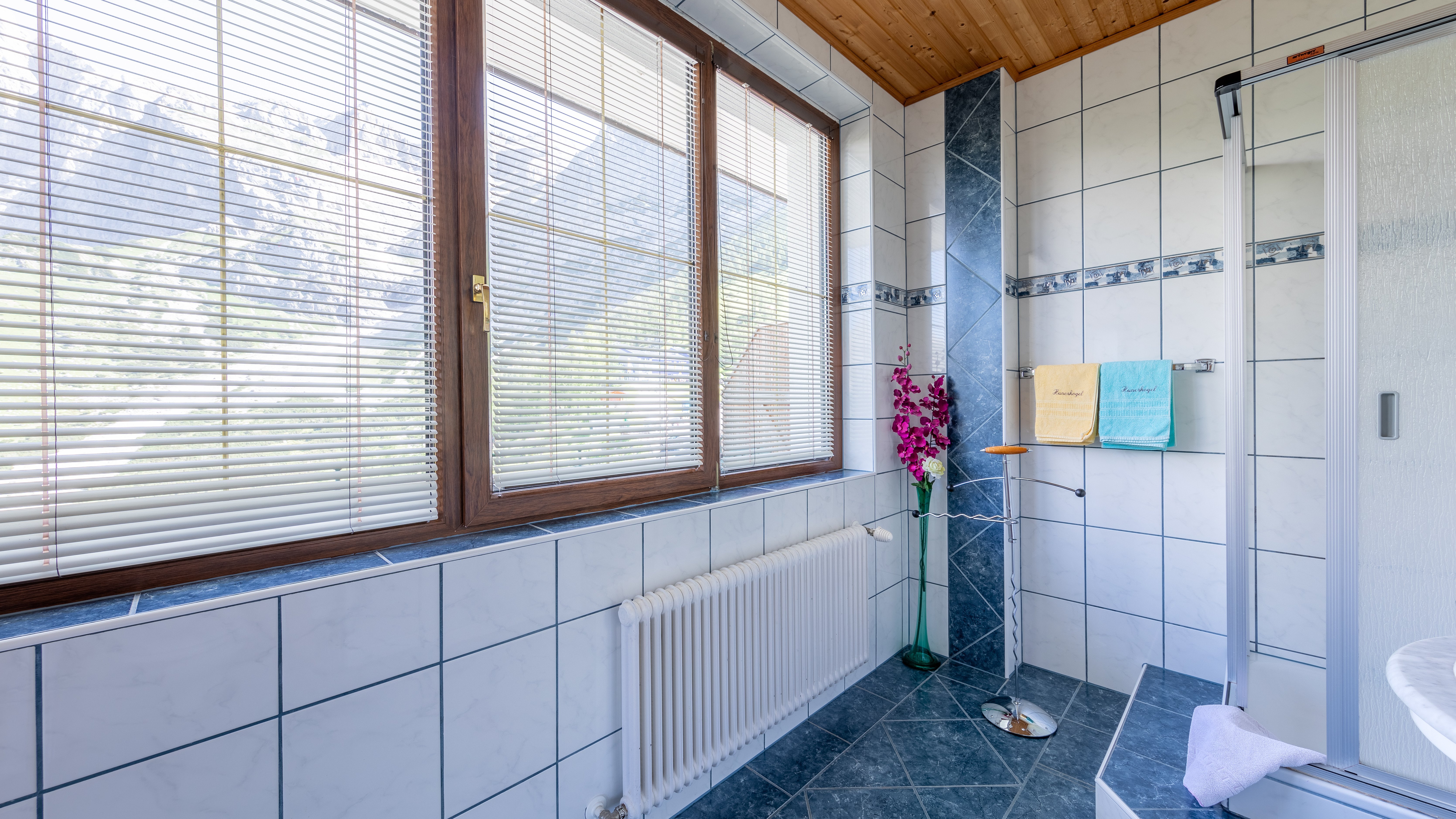 Badezimmer mit gefliesten Wänden und einer Dusche unter einem Fenster für Tageslicht.