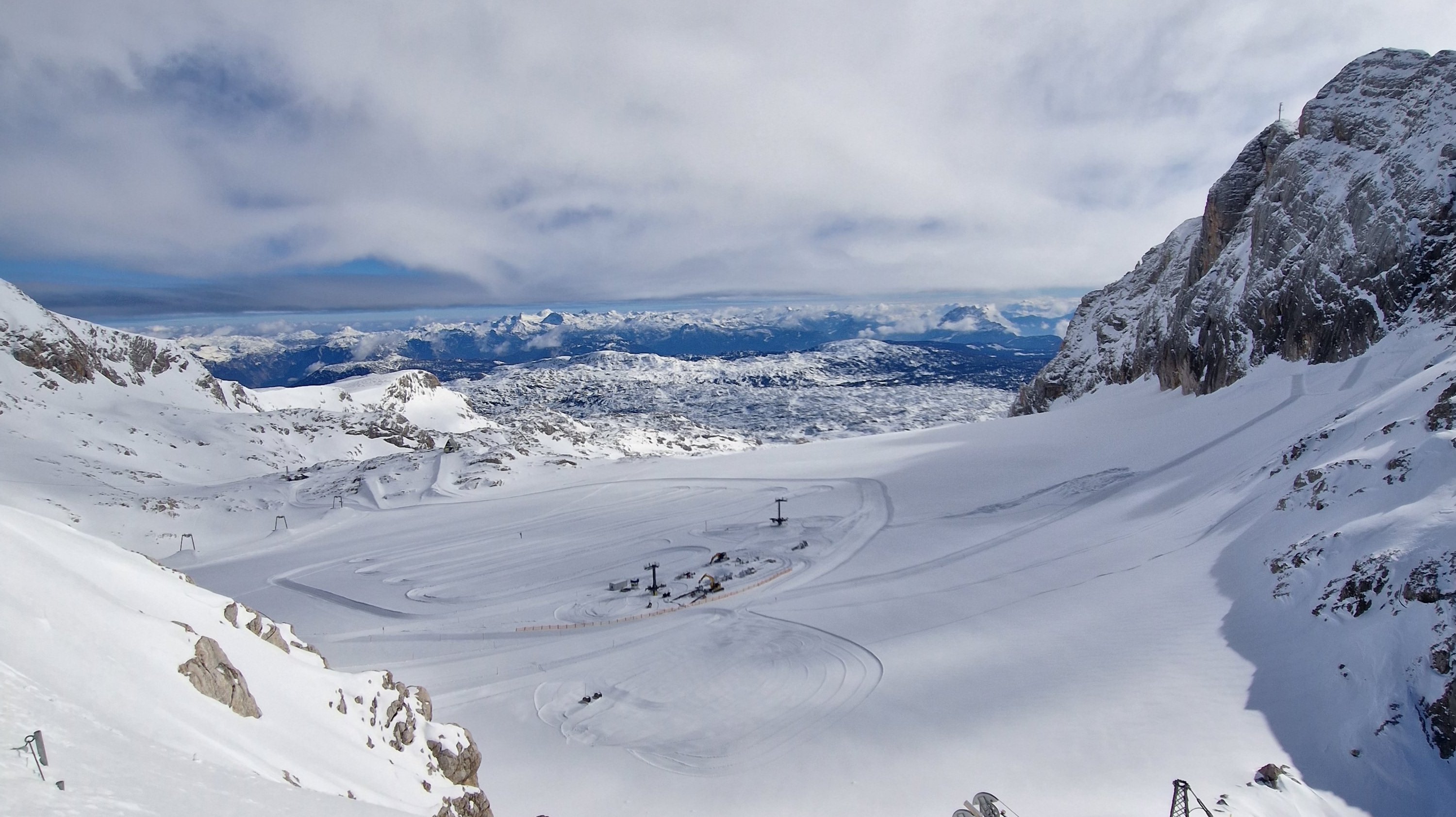 Schneebedeckte Landschaft mit Bergen und teilweise sichtbarem Skilift im Hintergrund