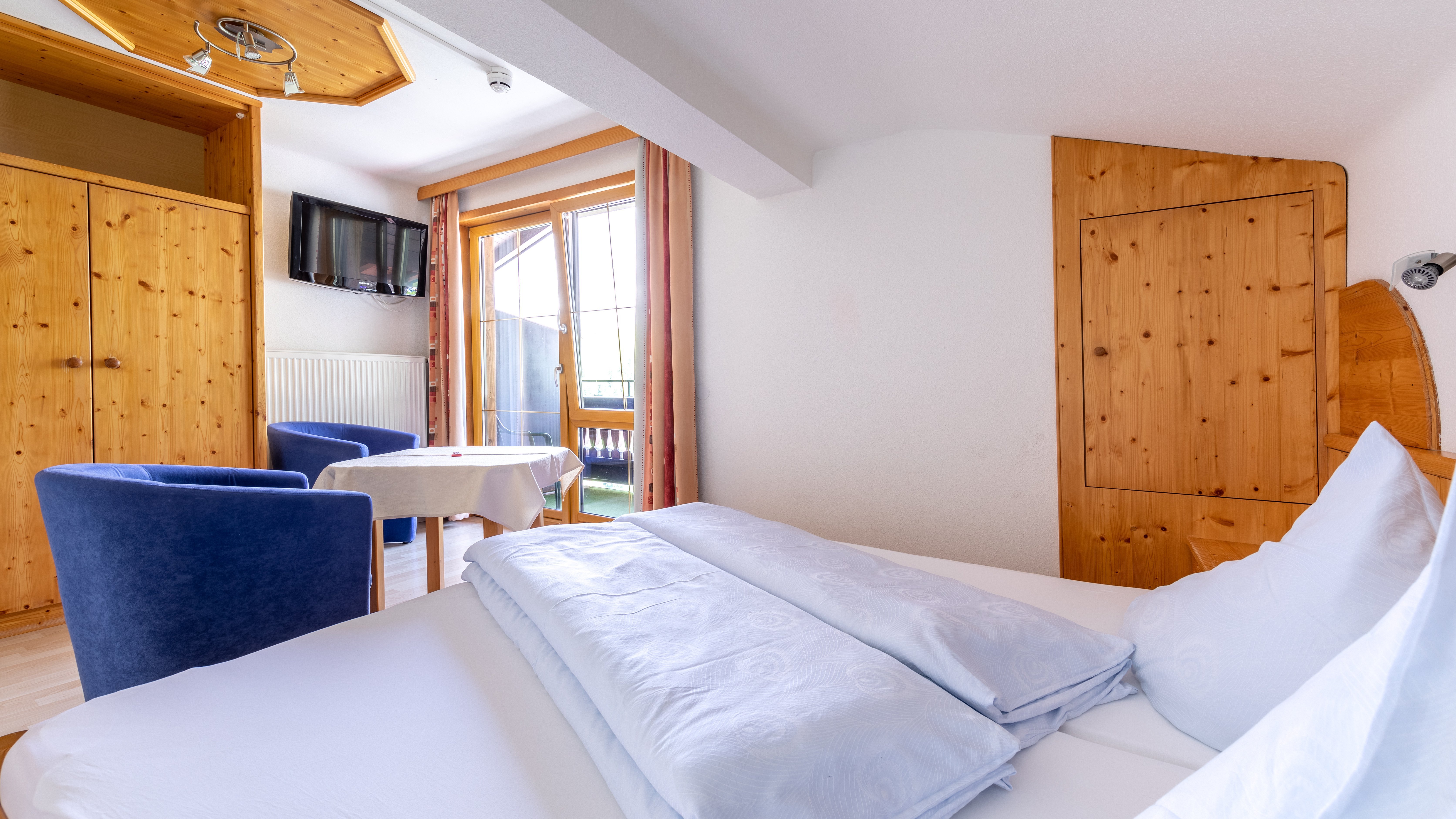 Hotelzimmer mit einem Doppelbett, Holz Möbeln und einer Sitzecke mit Tisch und Stühlen.