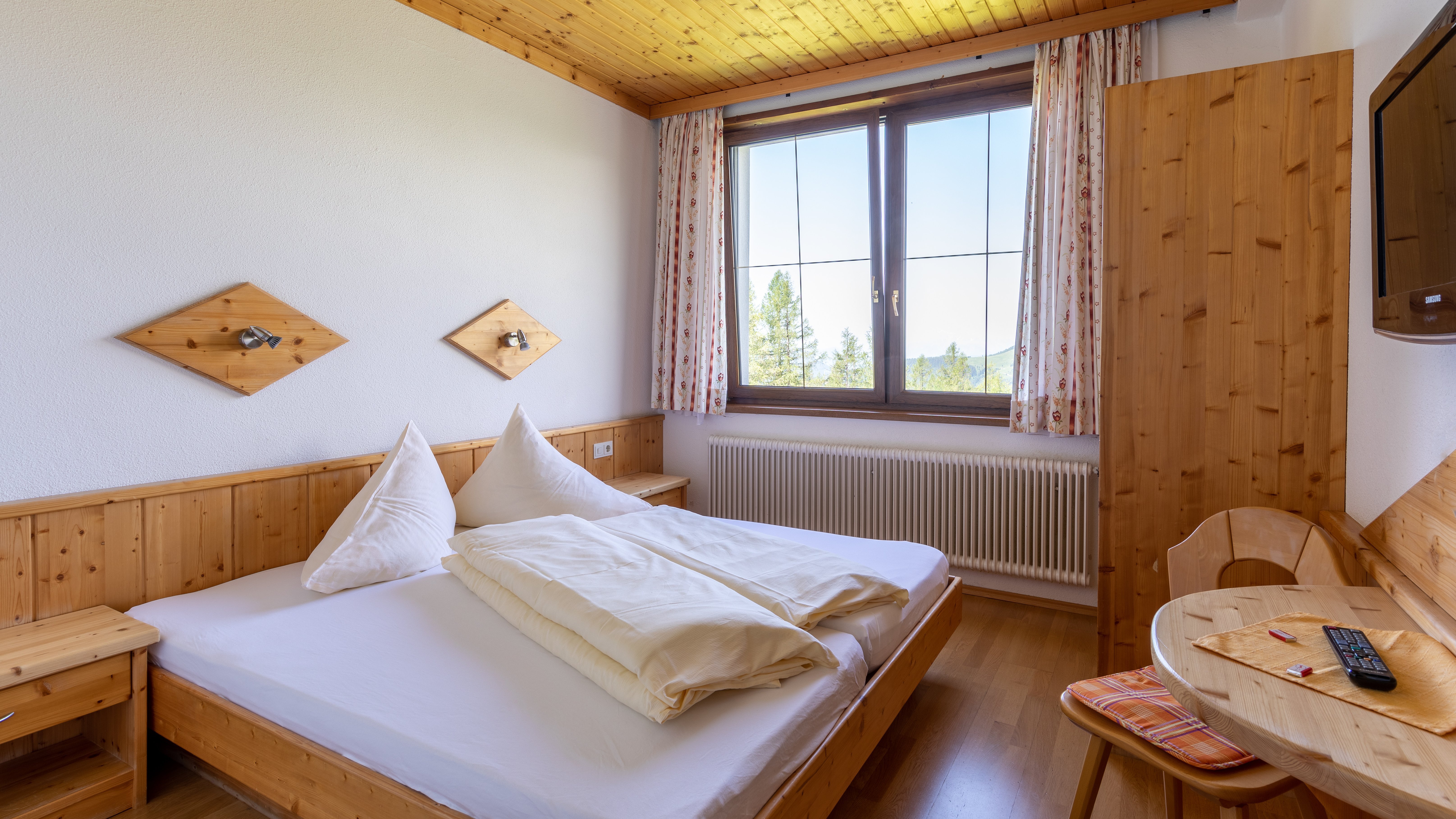 Hotelzimmer mit Holzinterieur und Blick auf die Berge durch ein großes Fenster, ordentliches Bett.