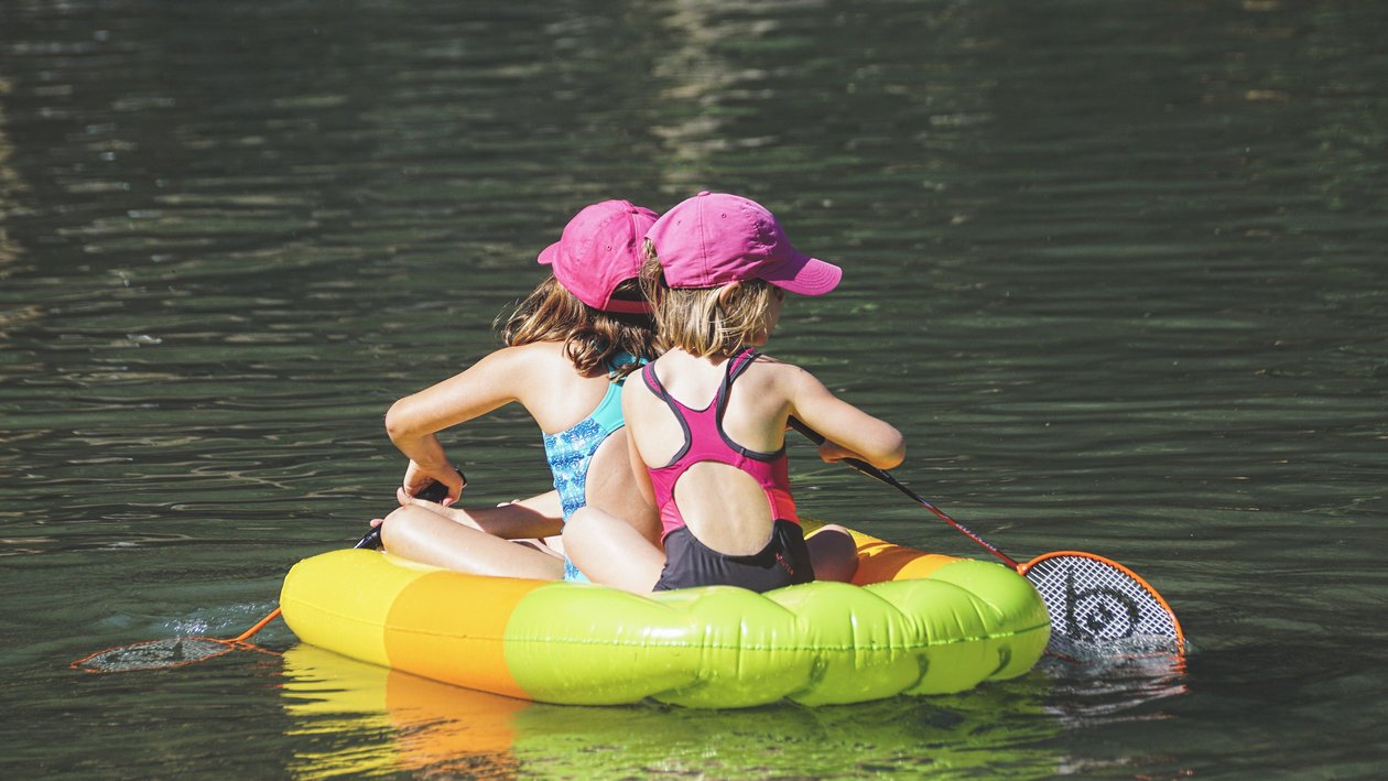 Badespaß auf dem Wasser Zwei Kinder sitzen auf einem bunten Luftboot im Wasser und genießen eine Sommeraktivität.