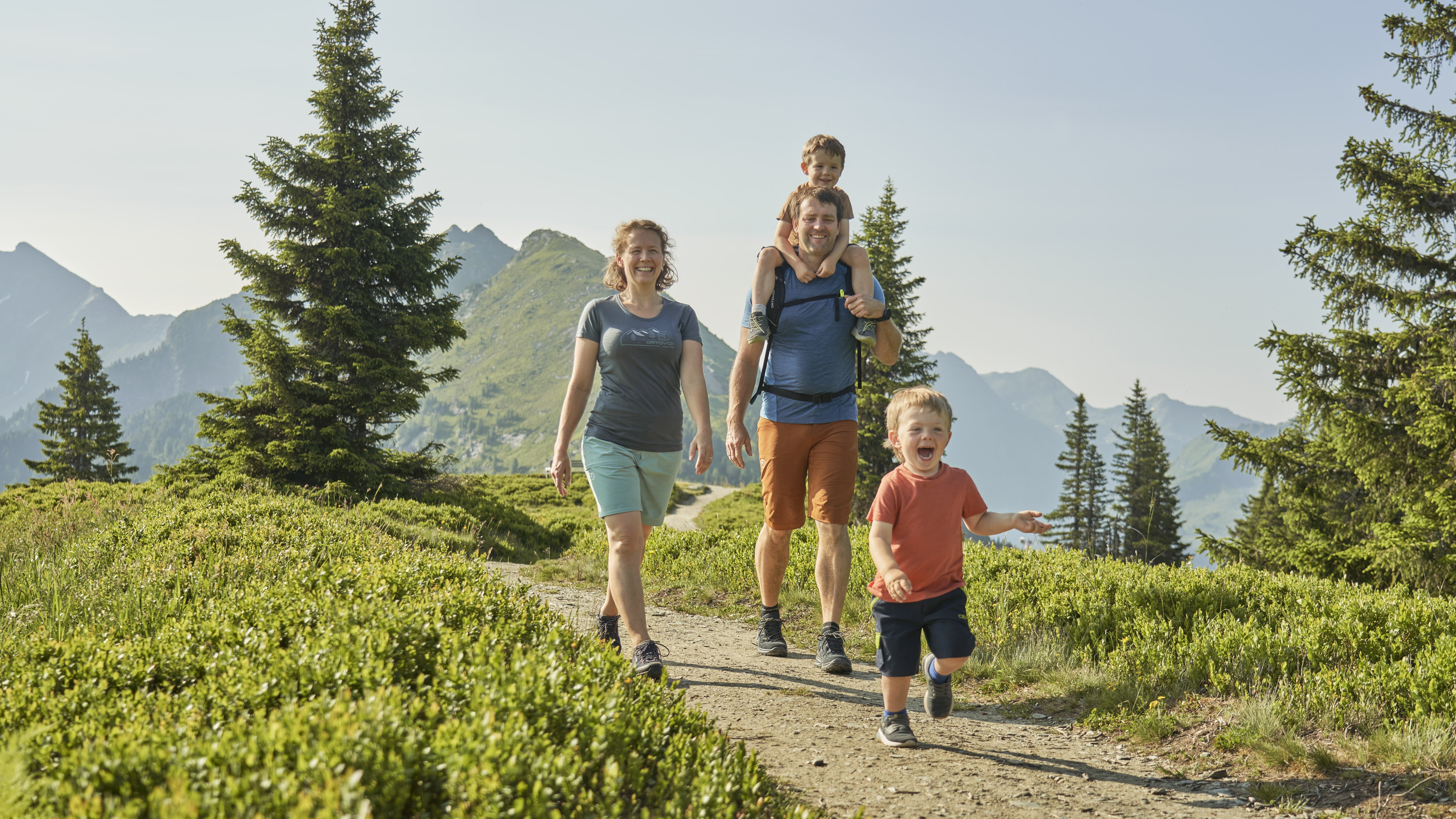 Familienabenteuer in den Bergen Eine Familie wandert auf einem malerischen Bergweg mit zwei Kindern und einem Elternteil.