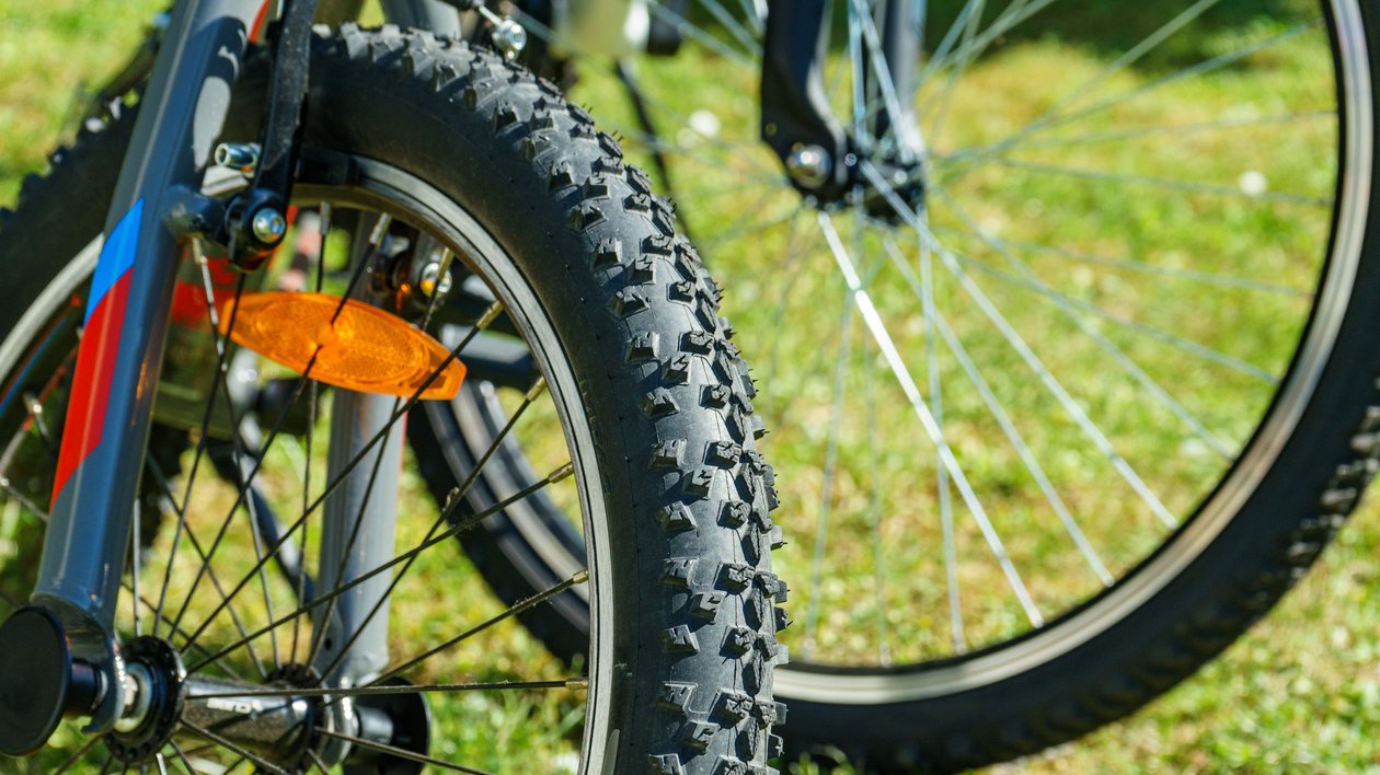 Close-up of a mountain bike tire resting on grass, showcasing tread pattern and wheel components