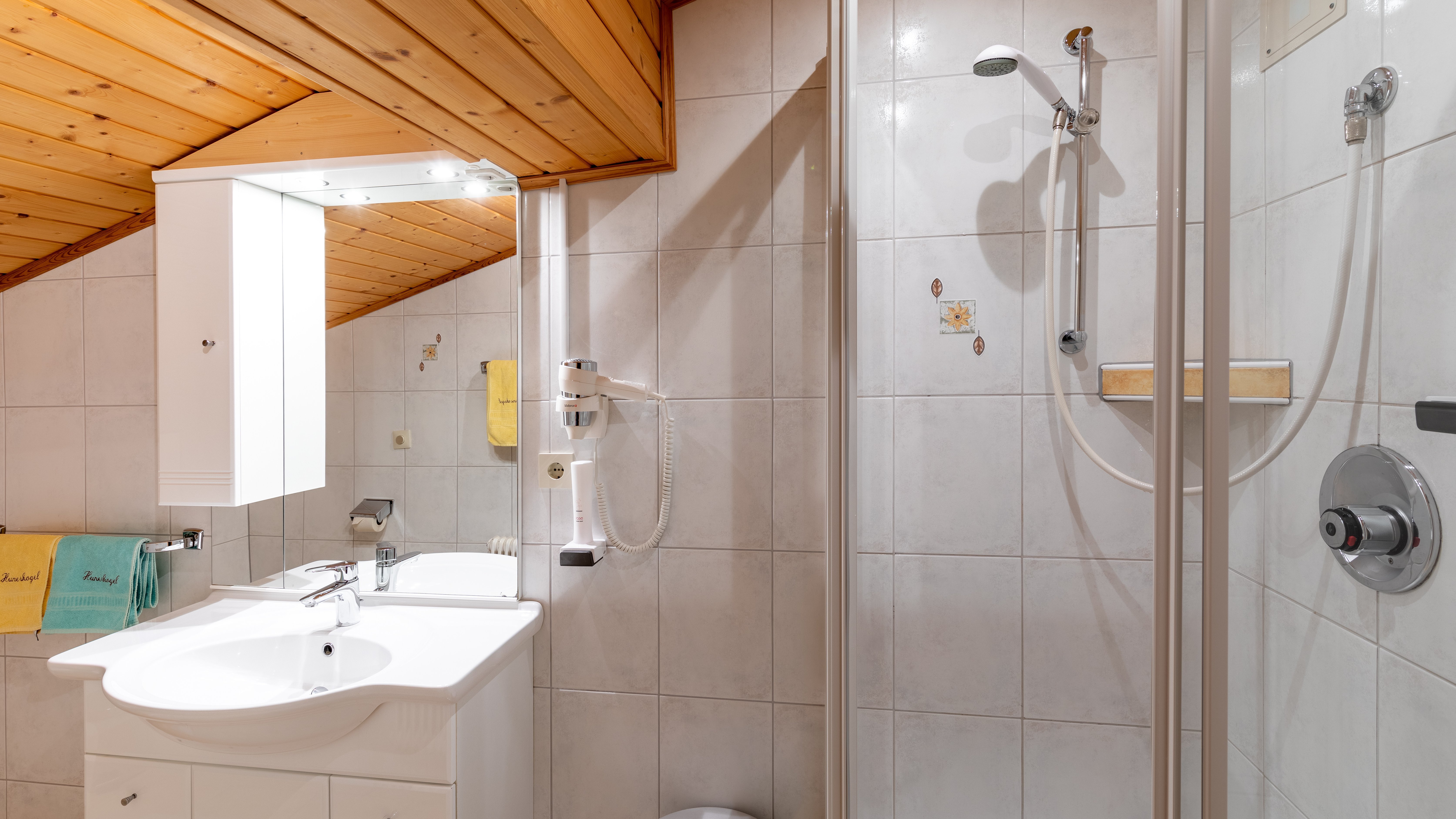 Helles Badezimmer mit Dusche, Waschbecken und Toilette sowie Holzdecke als Akzent.