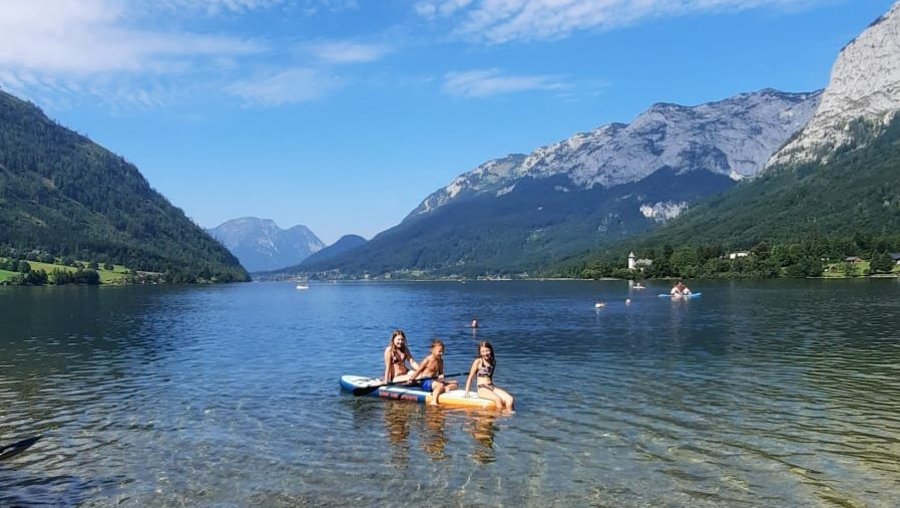 Two individuals kayaking on a tranquil lake surrounded by mountains and blue sky