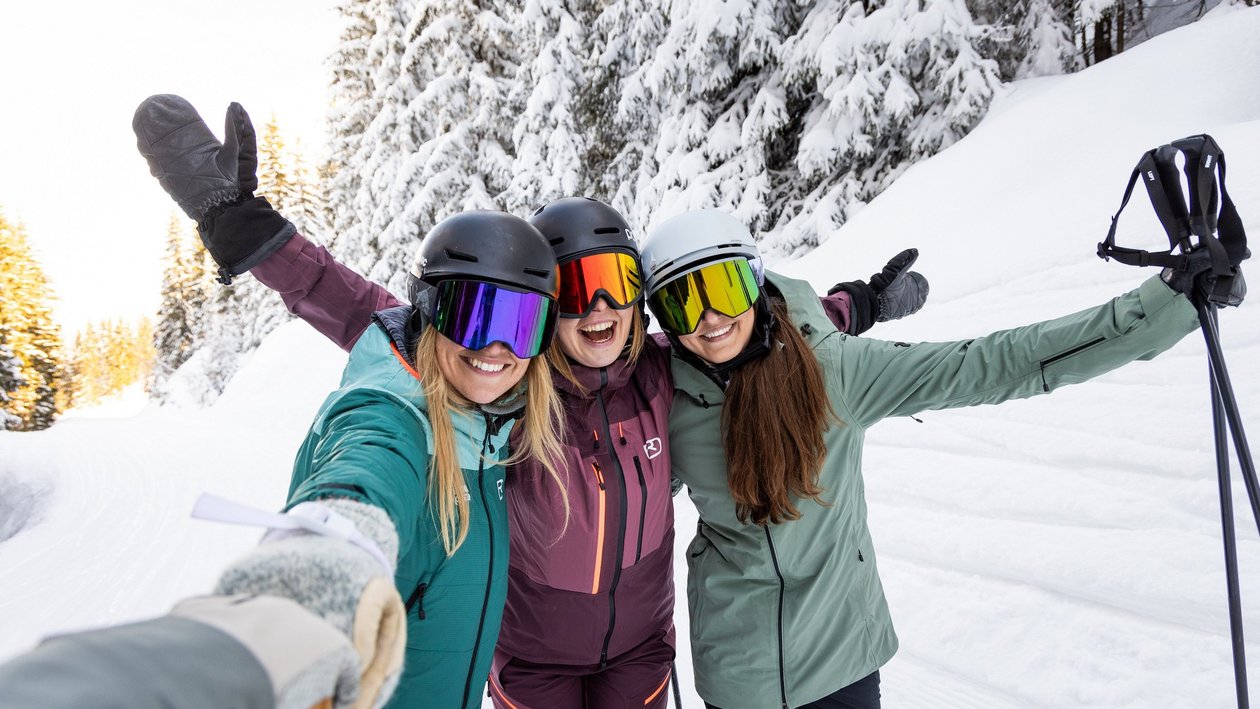 Schneevergnügen mit Freunden Drei Frauen stehen lächelnd im Schnee und posieren beim Skifahren in einer winterlichen Landschaft.