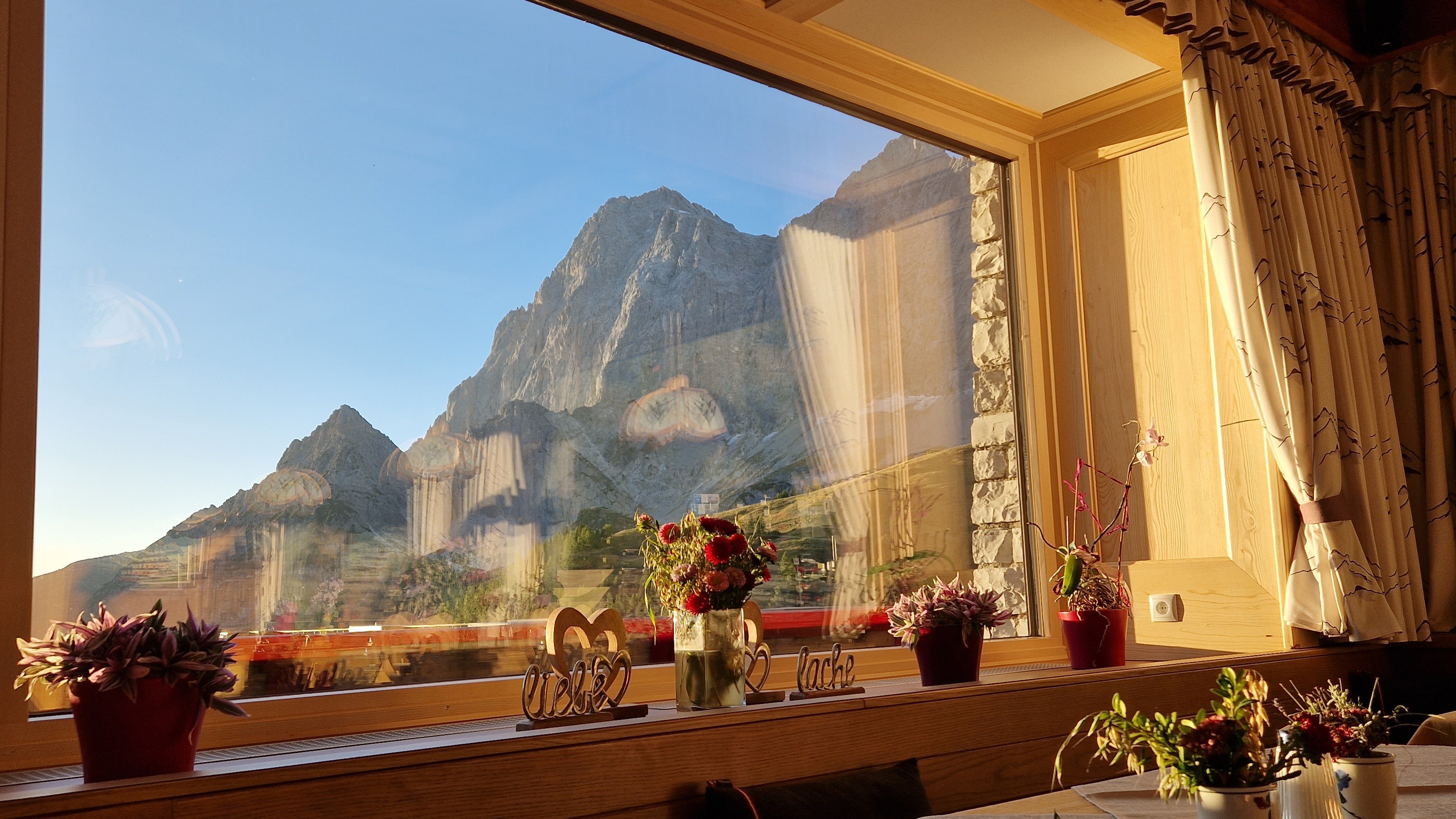 Interior space with a table set near a large window overlooking mountains and floral decorations