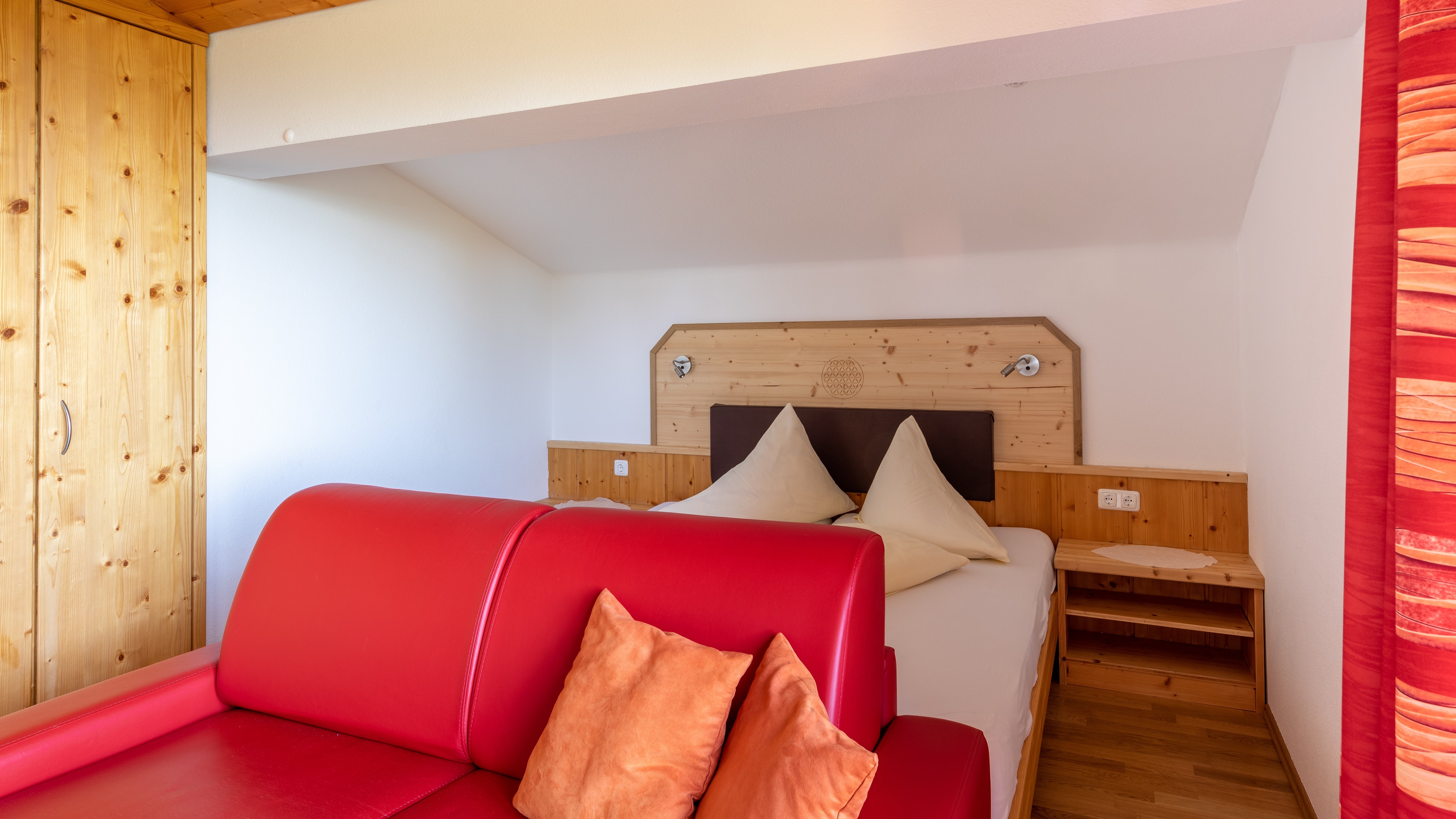 Ein modernes Hotelzimmer mit einem roten Sofa, einem Bett mit dekorativen Kissen und Holzelementen.