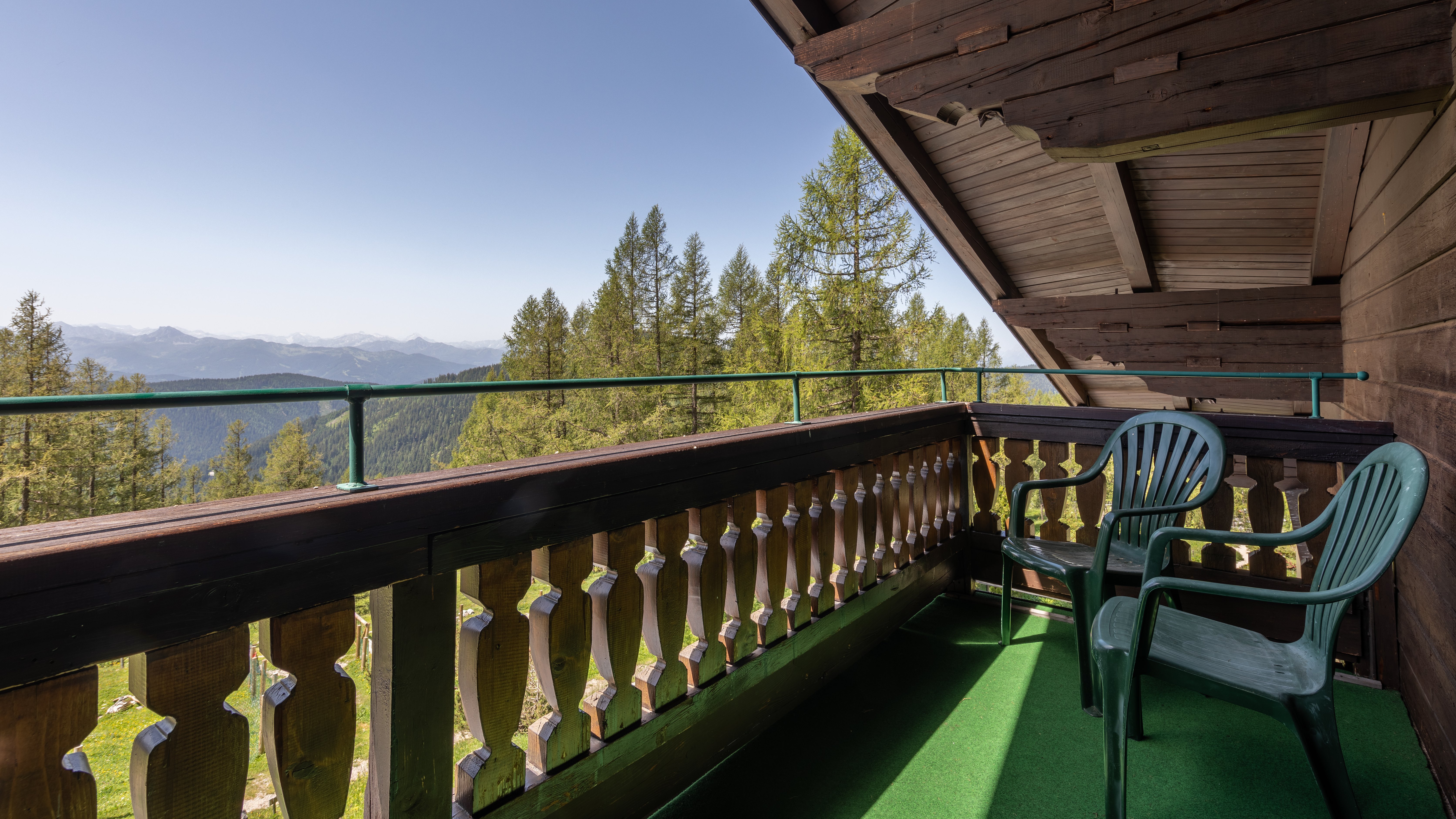 Balkon mit zwei grünen Stühlen, Aussicht auf eine Berglandschaft unter klarem Himmel