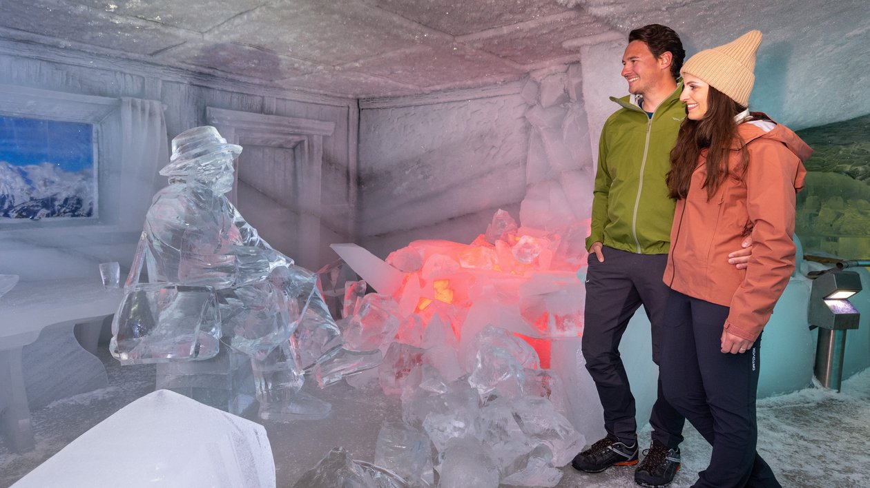 Paar im Eispalast Ein Paar steht in einem Raum mit Eisskulpturen und leuchtenden Elementen umgeben von Schnee.