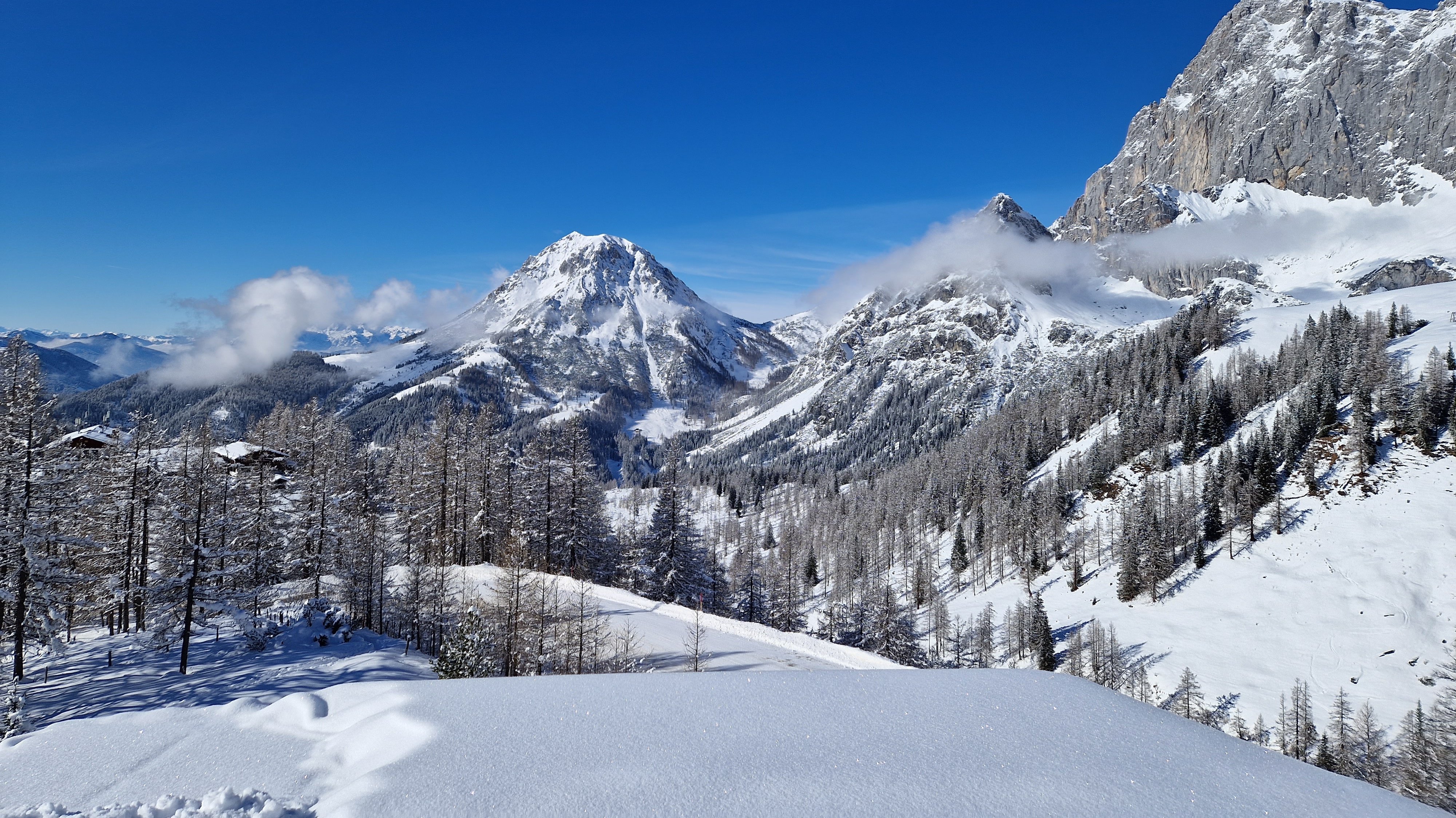 Schneebedeckte Berglandschaft Panoramablick auf eine schneebedeckte Berglandschaft mit klar blauem Himmel und bewaldetem Tal.