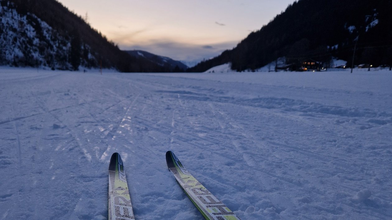 Pair of cross-country skis on a snowy trail with mountains and sunset in the background