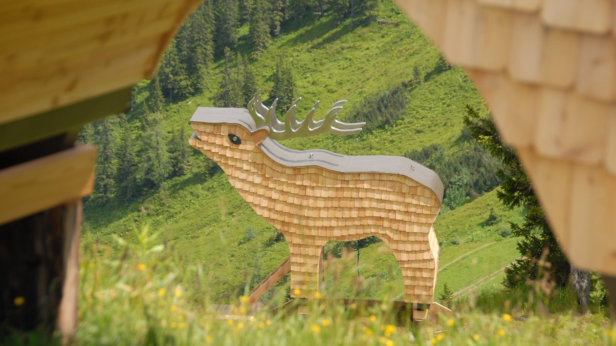 A large wooden deer sculpture surrounded by greenery and wooden structures in an outdoor setting.