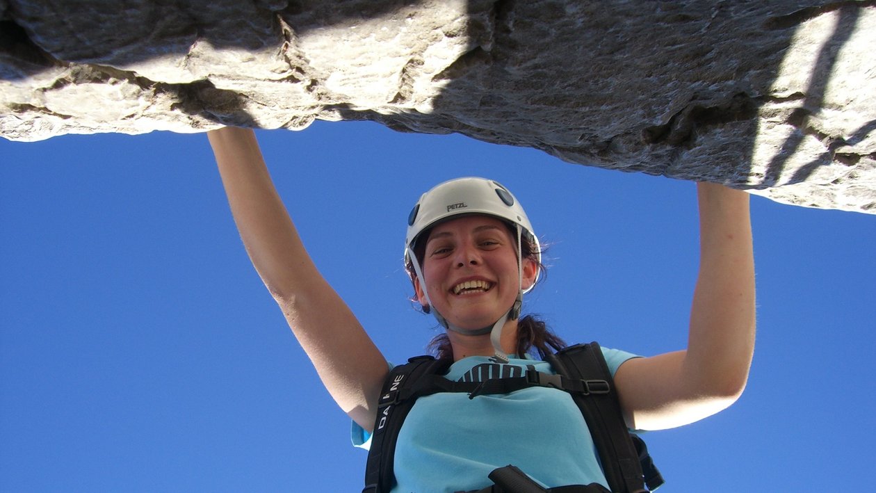 Abenteuer am Felsen Eine weibliche Kletterin hält sich an einem Felsvorsprung fest und lächelt, während sie Kletterausrüstung trägt.