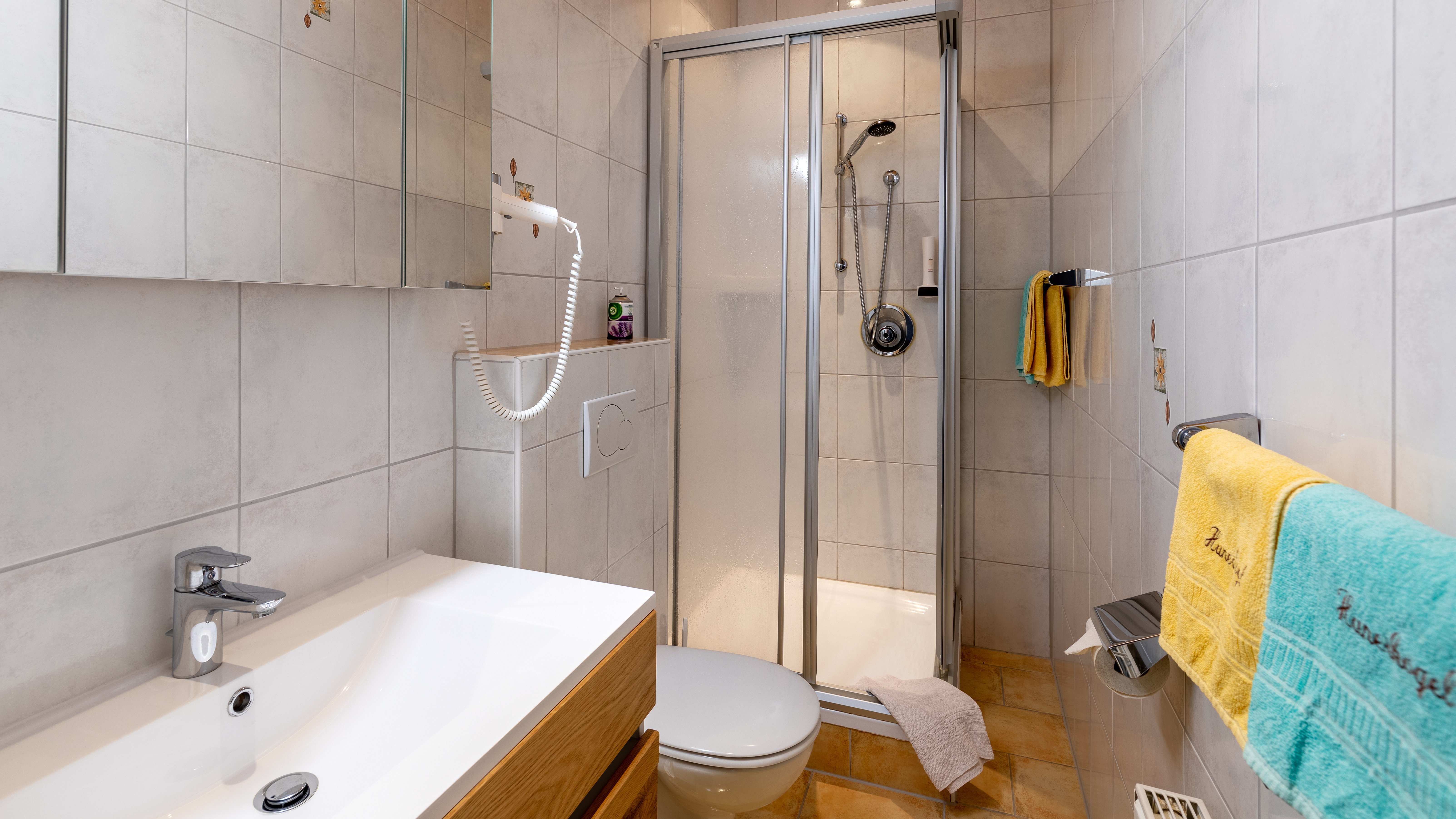 Badezimmer mit Duschbereich, Waschbecken und Holzschrank in elegantem Design und gefliesten Wänden.
