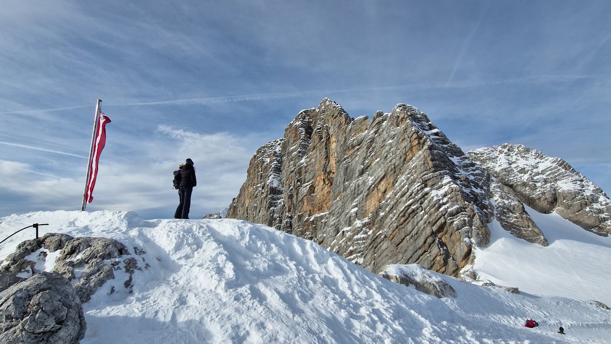 Abenteuer am Gipfel Person steht auf schneebedecktem Berggipfel mit Felsen und amerikanischer Flagge.