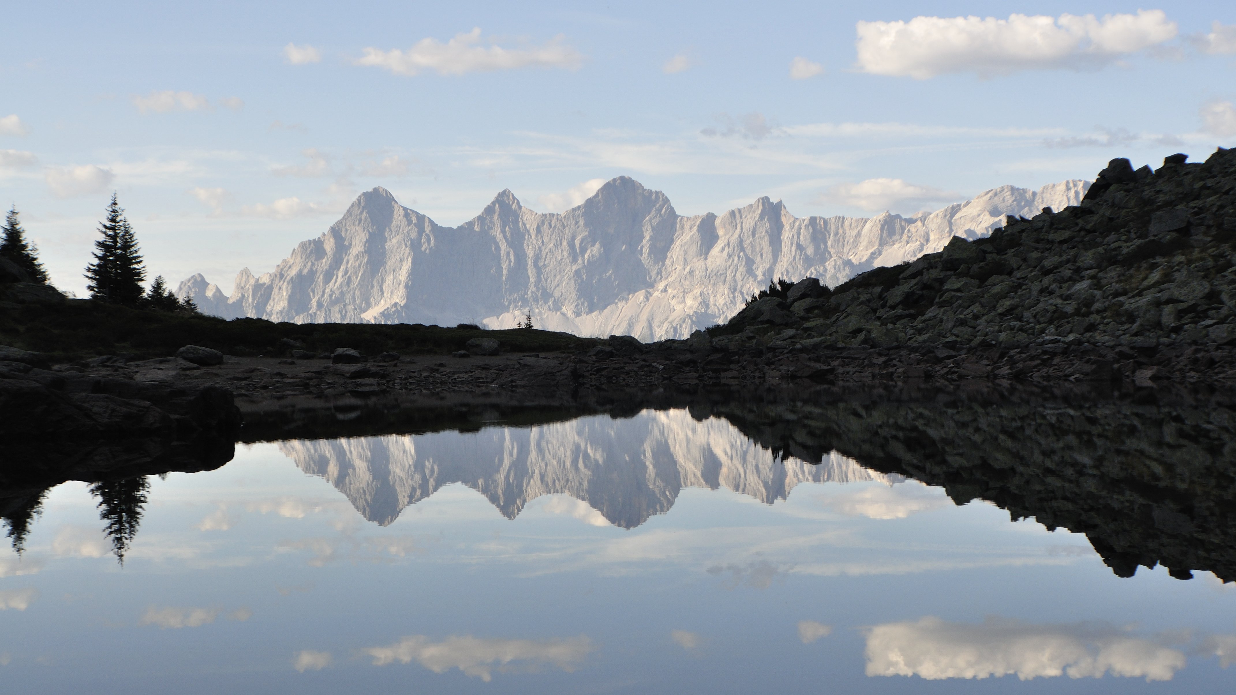 Berglandschaft mit Spiegelung im Wasser Berge spiegeln sich in einem ruhigen Gewässer unter klarem Himmel und Wolkenbedeckung
