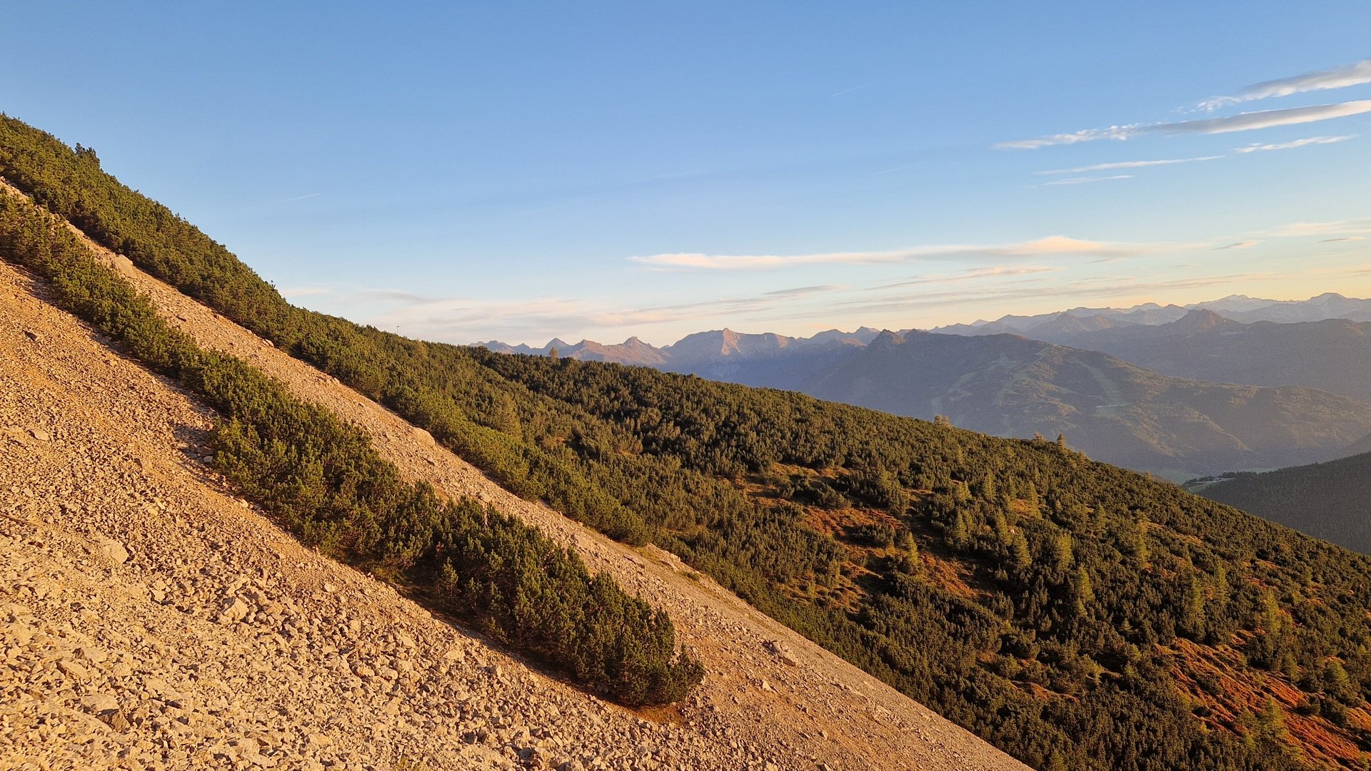 Berglandschaft mit bewachsenen Hängen und Sonnenuntergang im Hintergrund, ideal für Wanderer