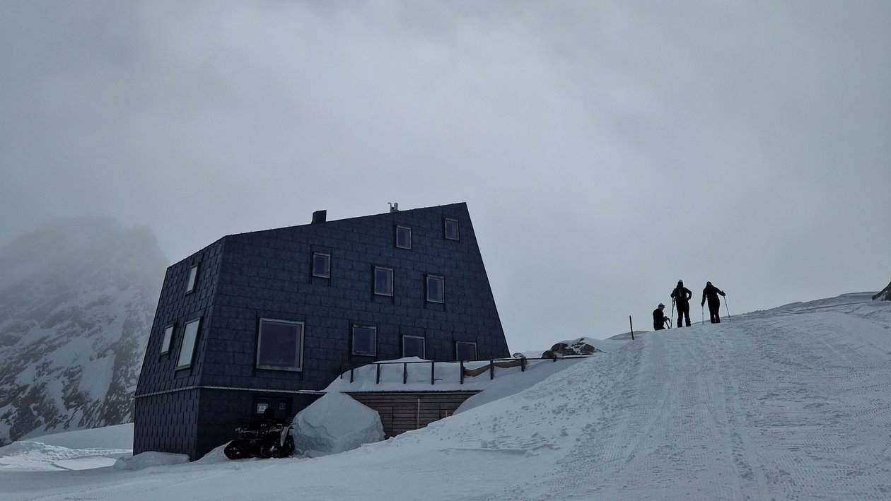 Moderne Berghütte im Winter Eine moderne Berghütte in einer verschneiten Landschaft mit zwei Wanderern auf dem Weg zur Hütte.