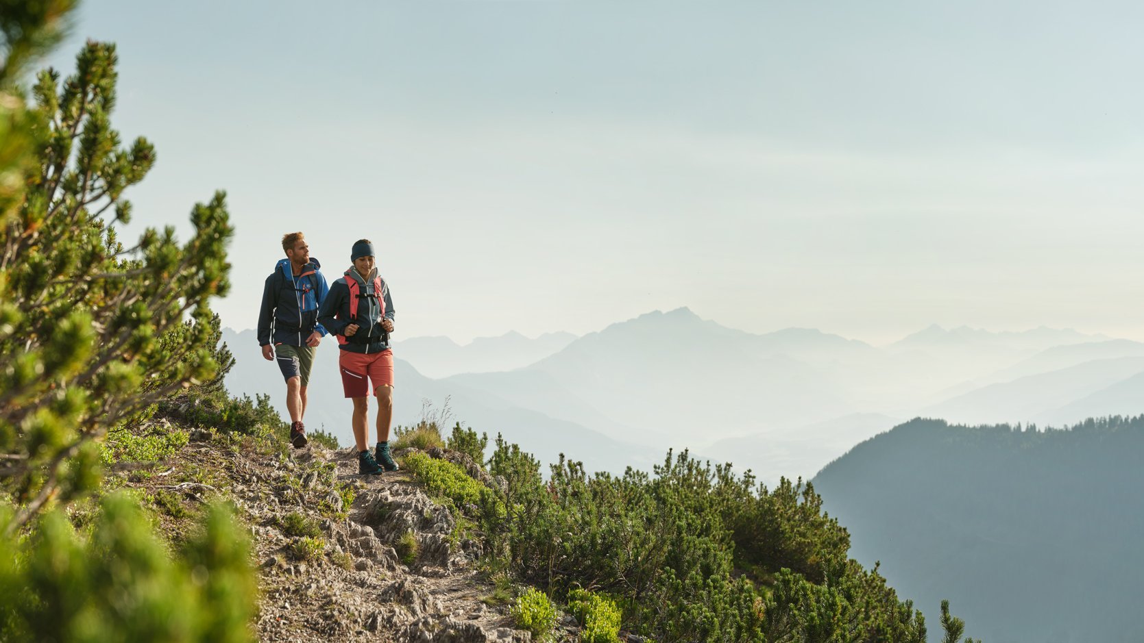 Zwei Wanderer auf einem steinigen Pfad in den Bergen, umgeben von Natur und grünen Wiesen.